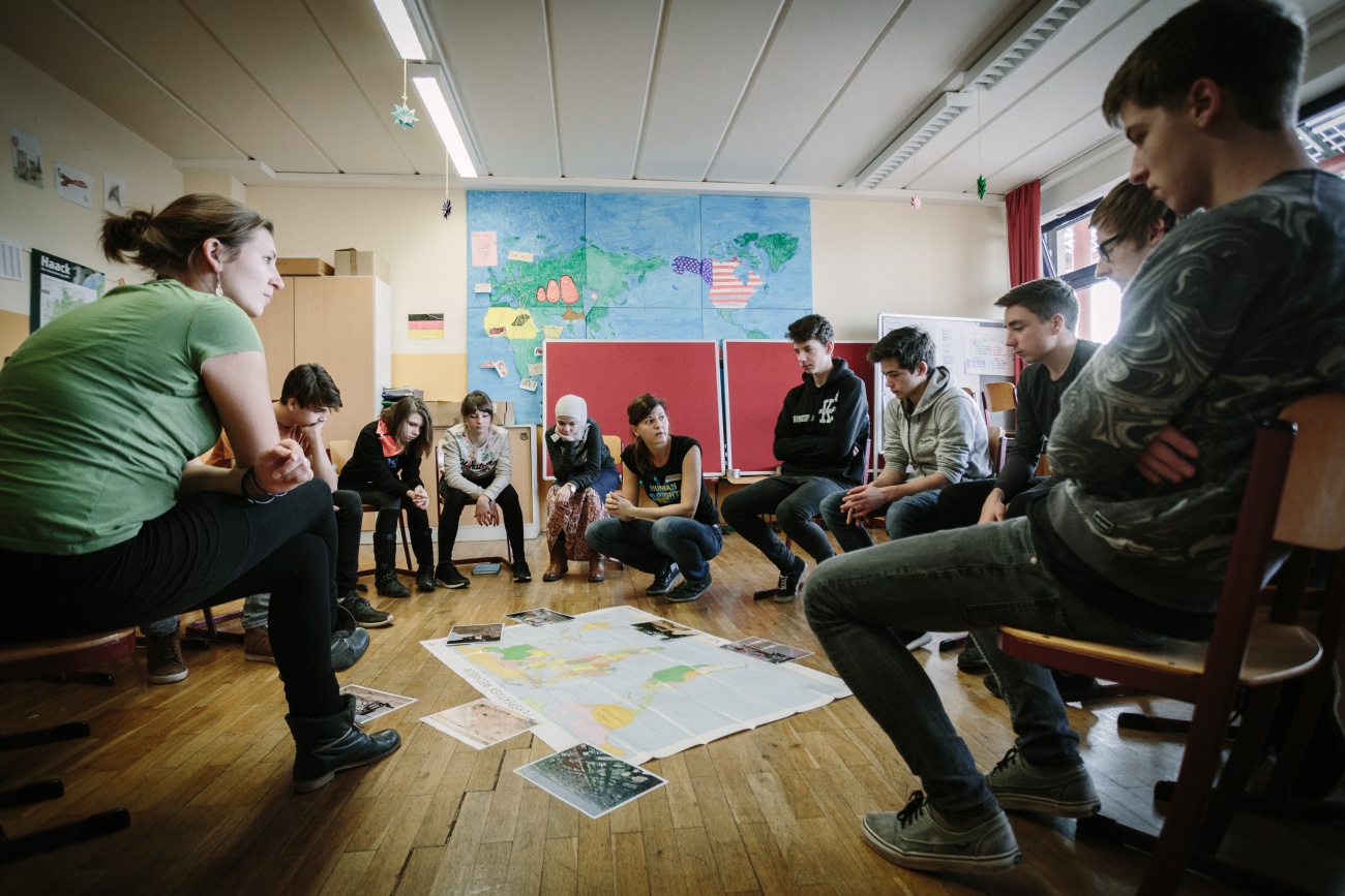 Blick in ein Klassenzimmer, Jugendliche im Stuhlkrei, in der Mitte eine Weltkarte