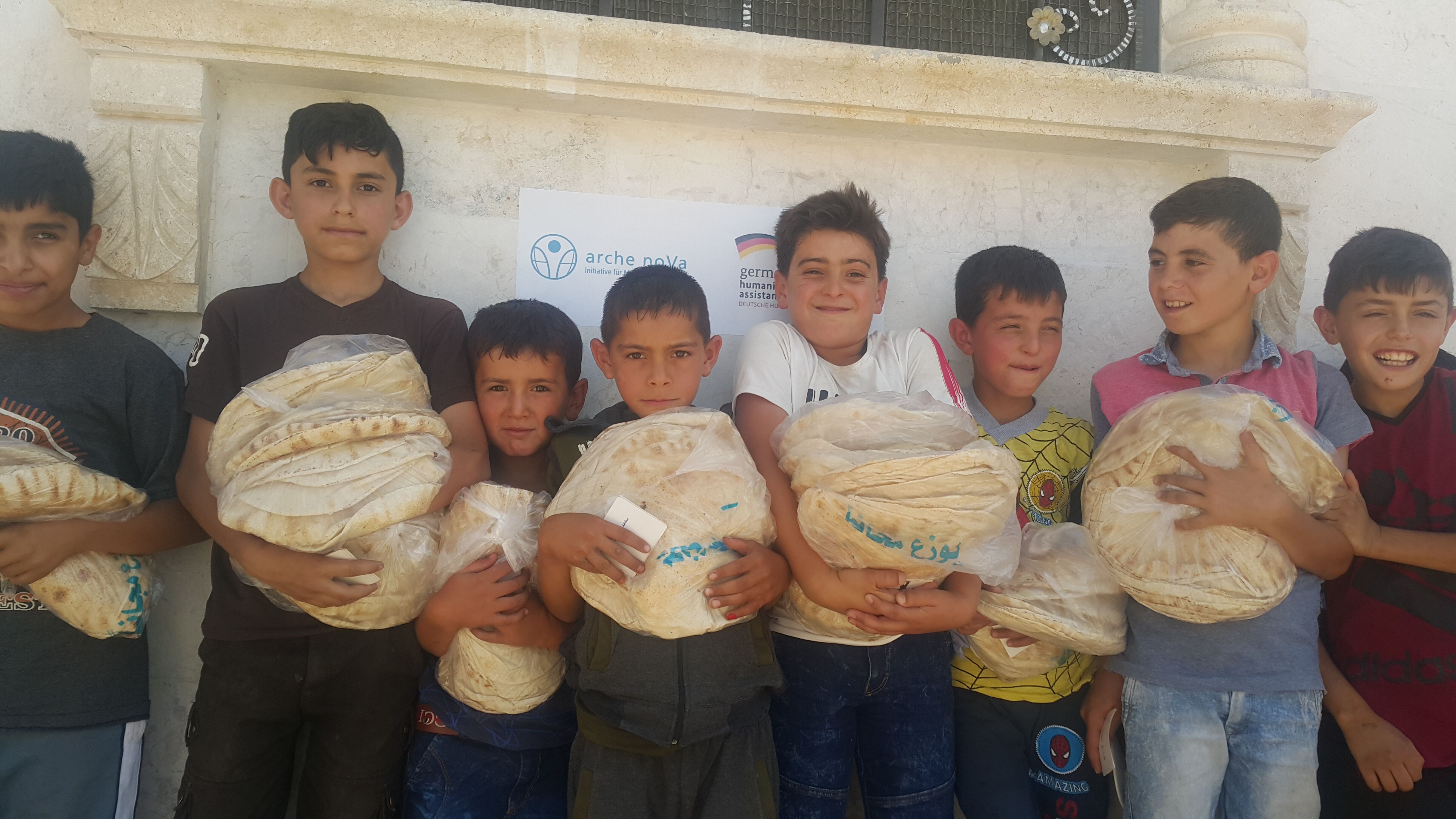 Jungen stehen in einer Reihe an einer Wand mit Brot im Arm