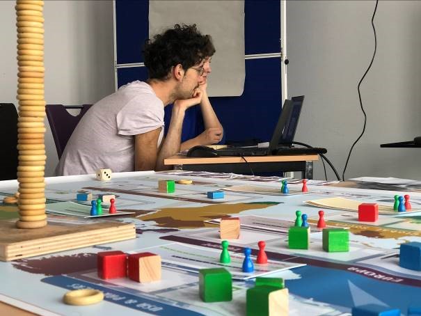 Zwei Teamenden arbeiten am Computer, vor ihnen ein Spielfeld 