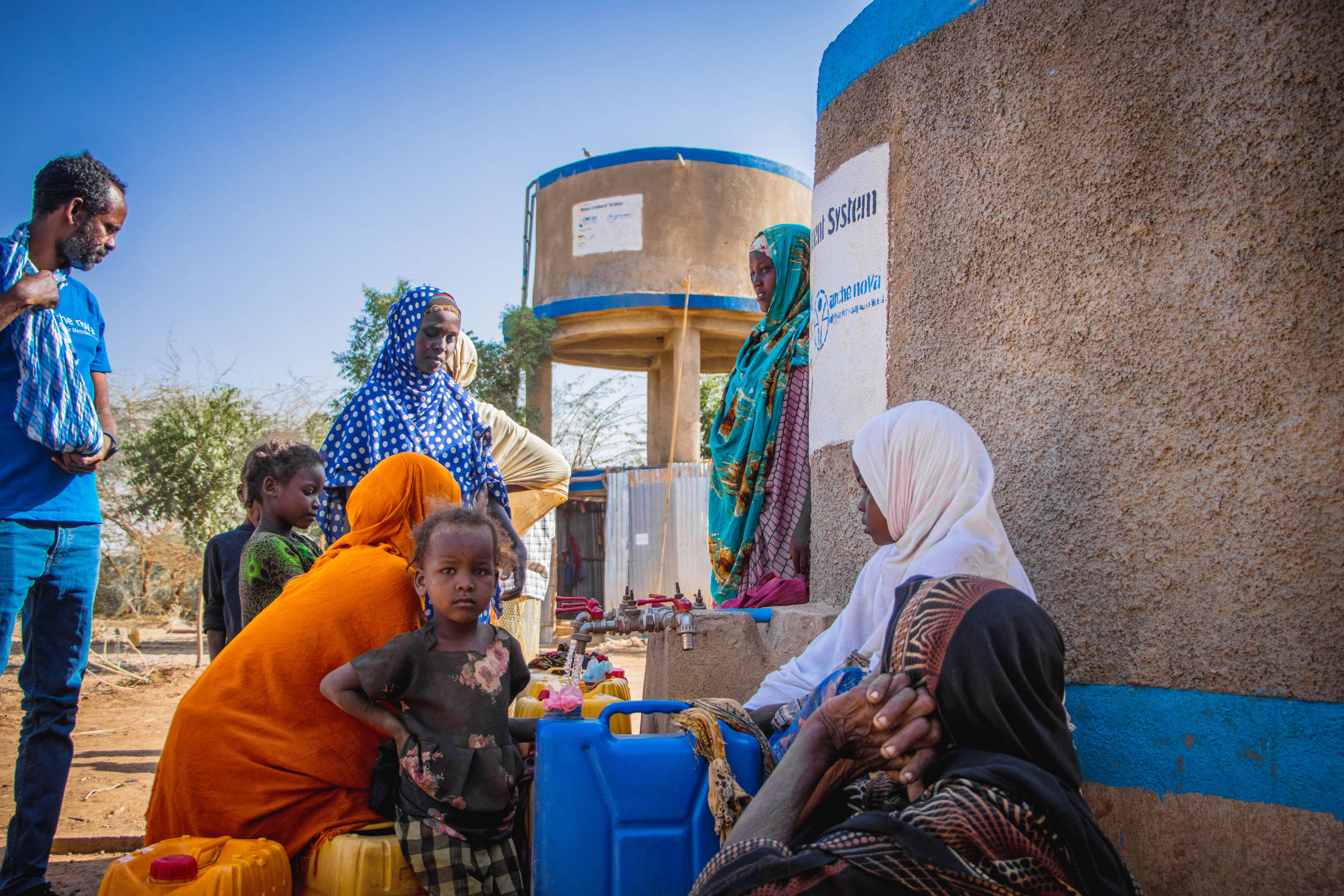 Menschgruppe an an Wasserausgabestation, Kind blickt in die Kamera