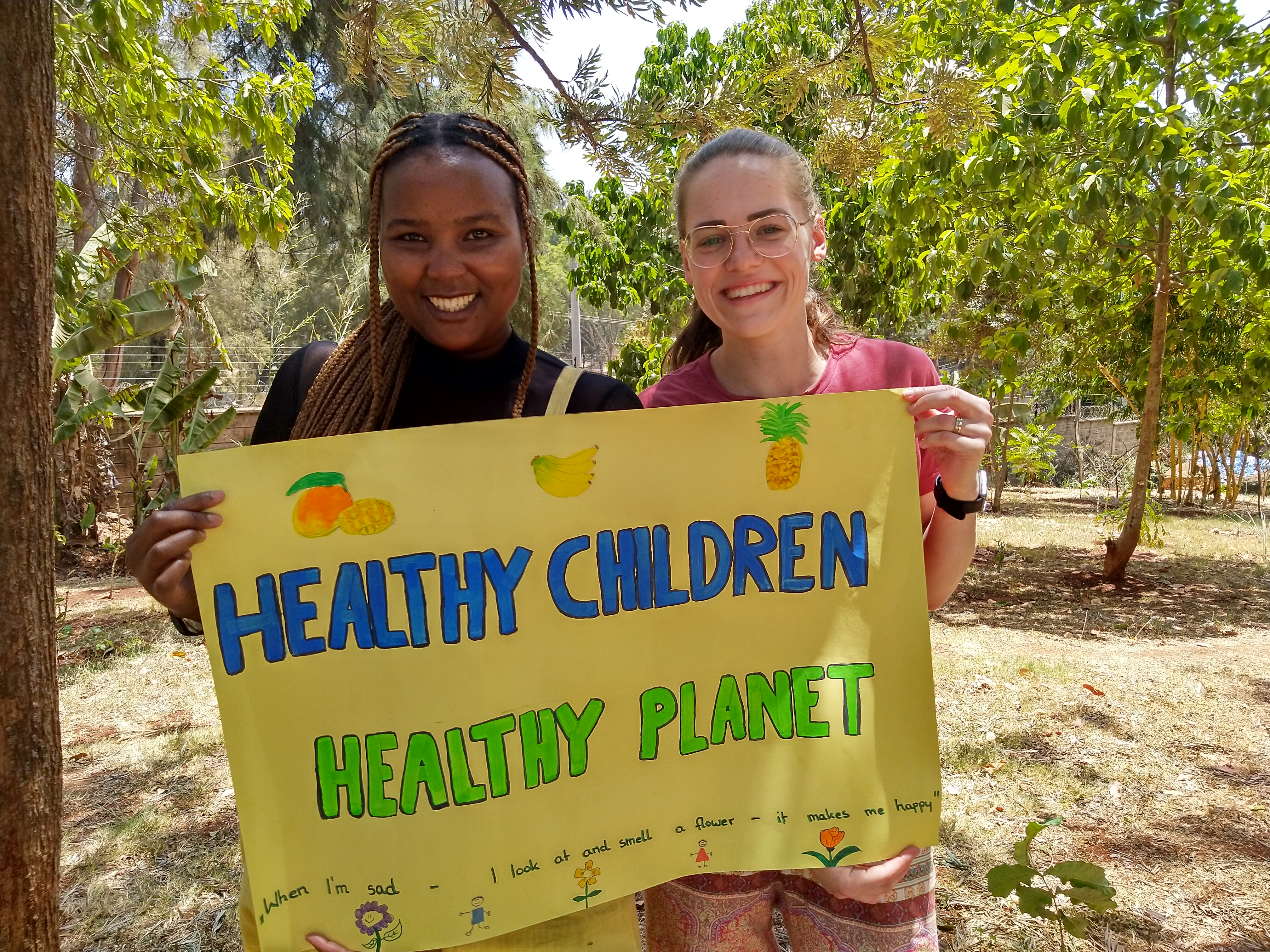 Das Bild zeigt zwei junge Frauen. Sie halten ein Plakat, auf dem „Healthy Children, healthy Planet“ steht.