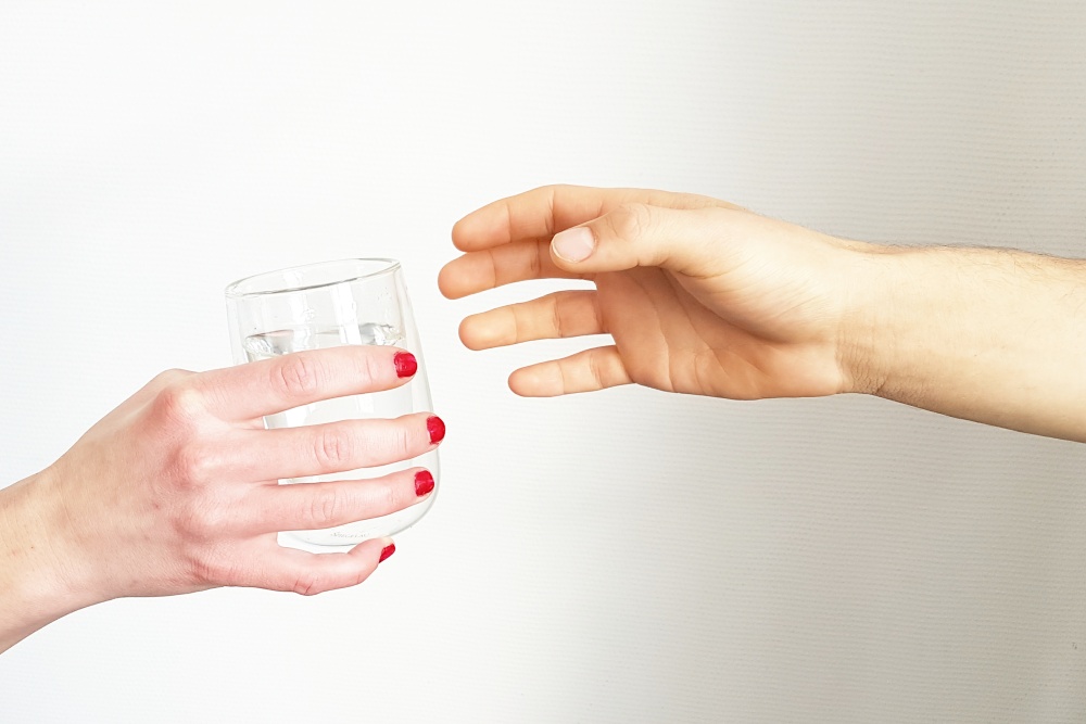 Hand mit rot lackierten Fingernägeln reicht einer zweiten Hand ein Glas Wasser