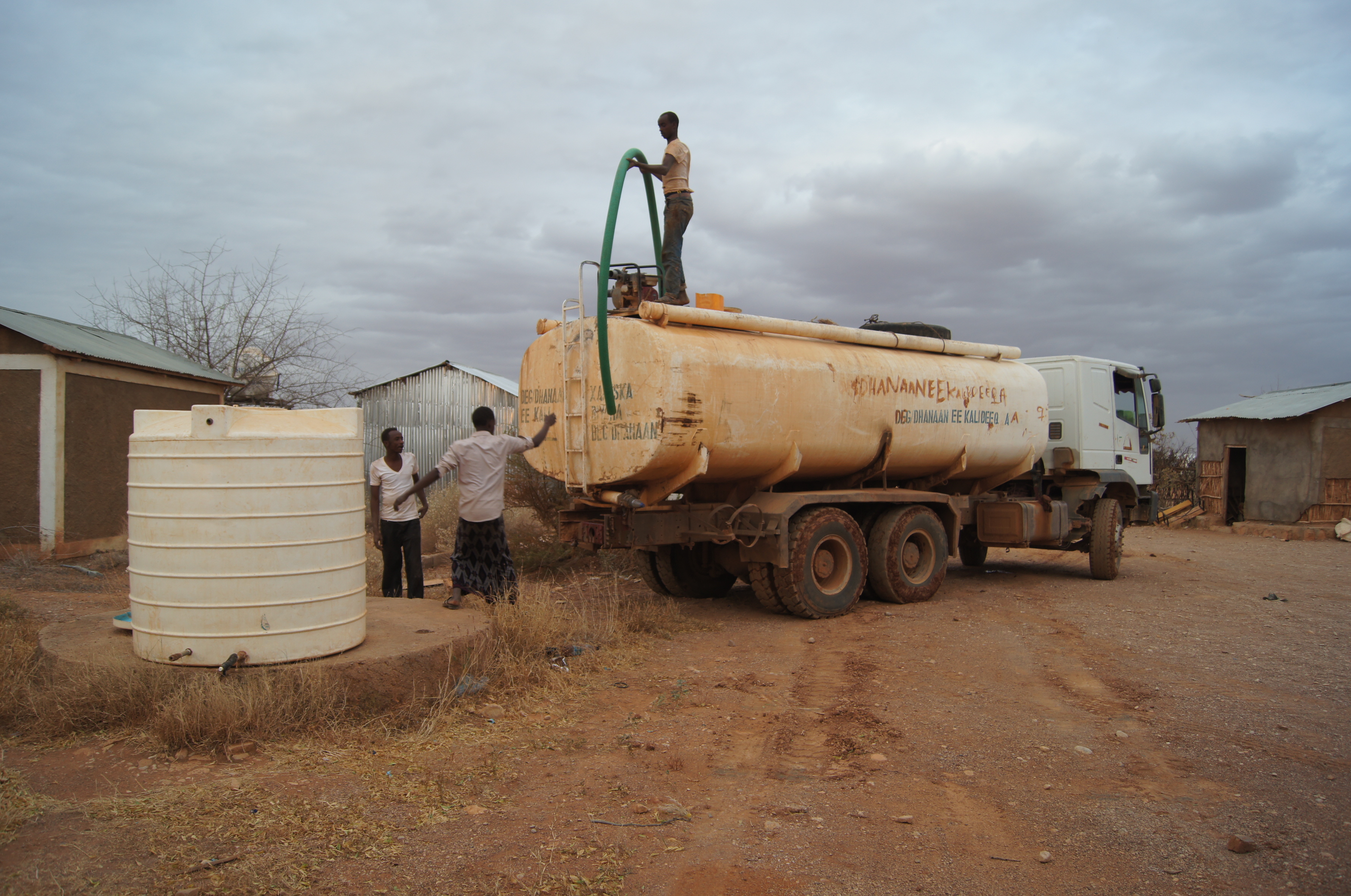 Ein Tanklastwagen steht rückwärts vor einem Wassertank. Auf dem Dach des Wagens hält ein Mann einen Schlauch mit großem Durchmesser.