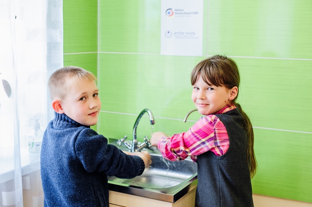 Junge und Mädchen waschen sich die Hände am Wasserhahn