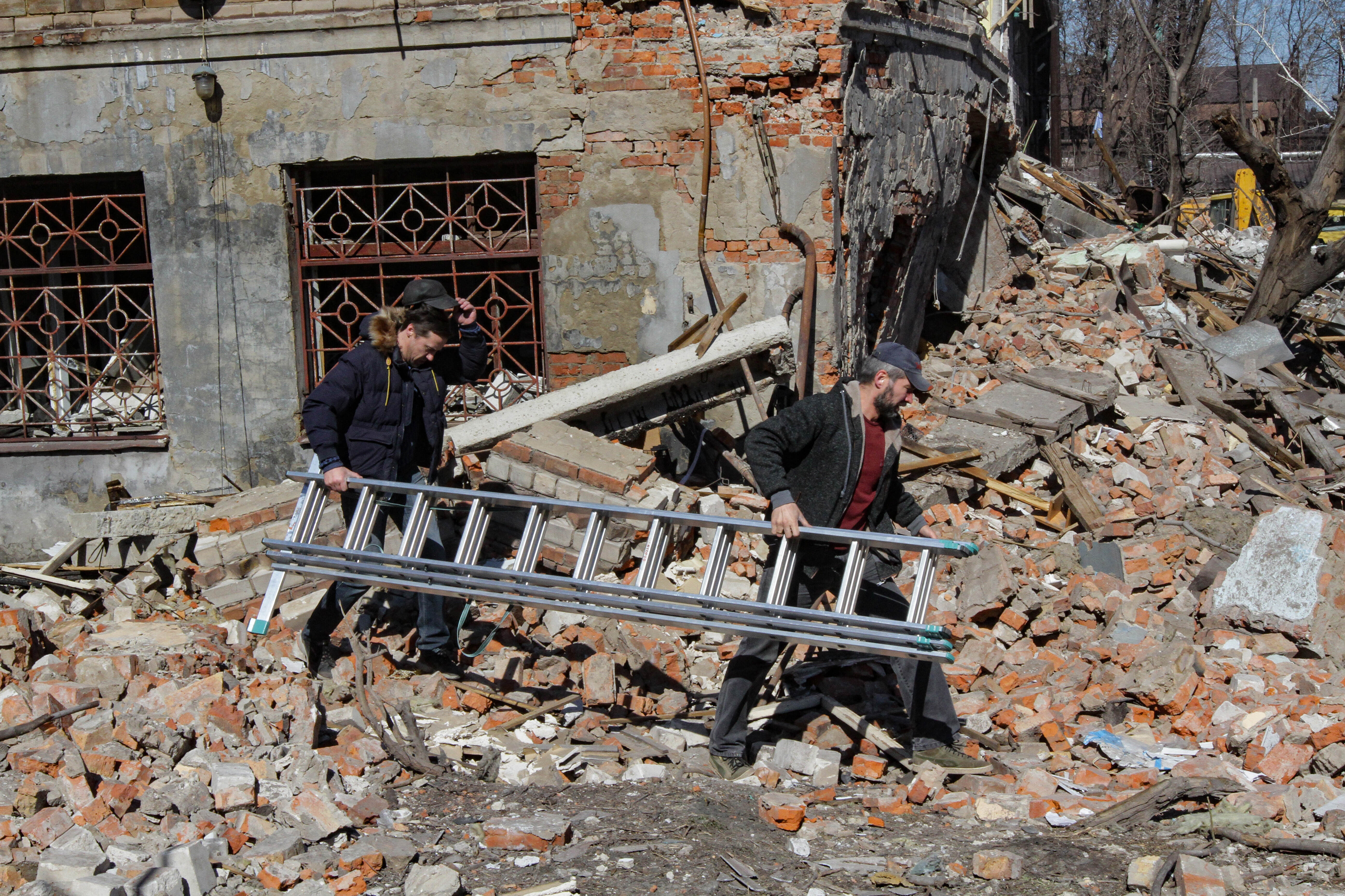 Menschen tragen eine Leiter vor zerstörtem Haus in Dnipro