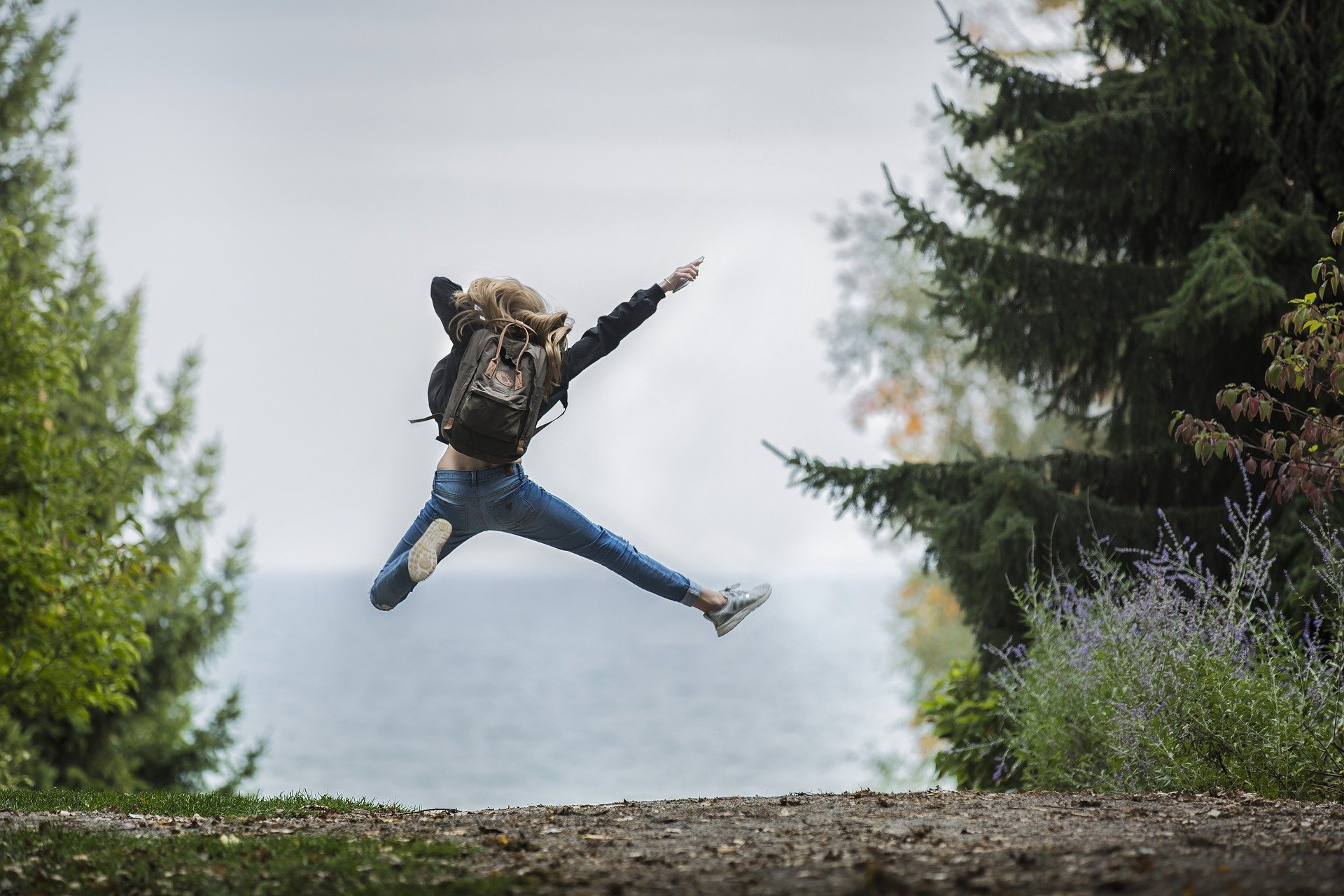 jugendliches Mädchen springt auf Waldweg ausgelassen in die Luft