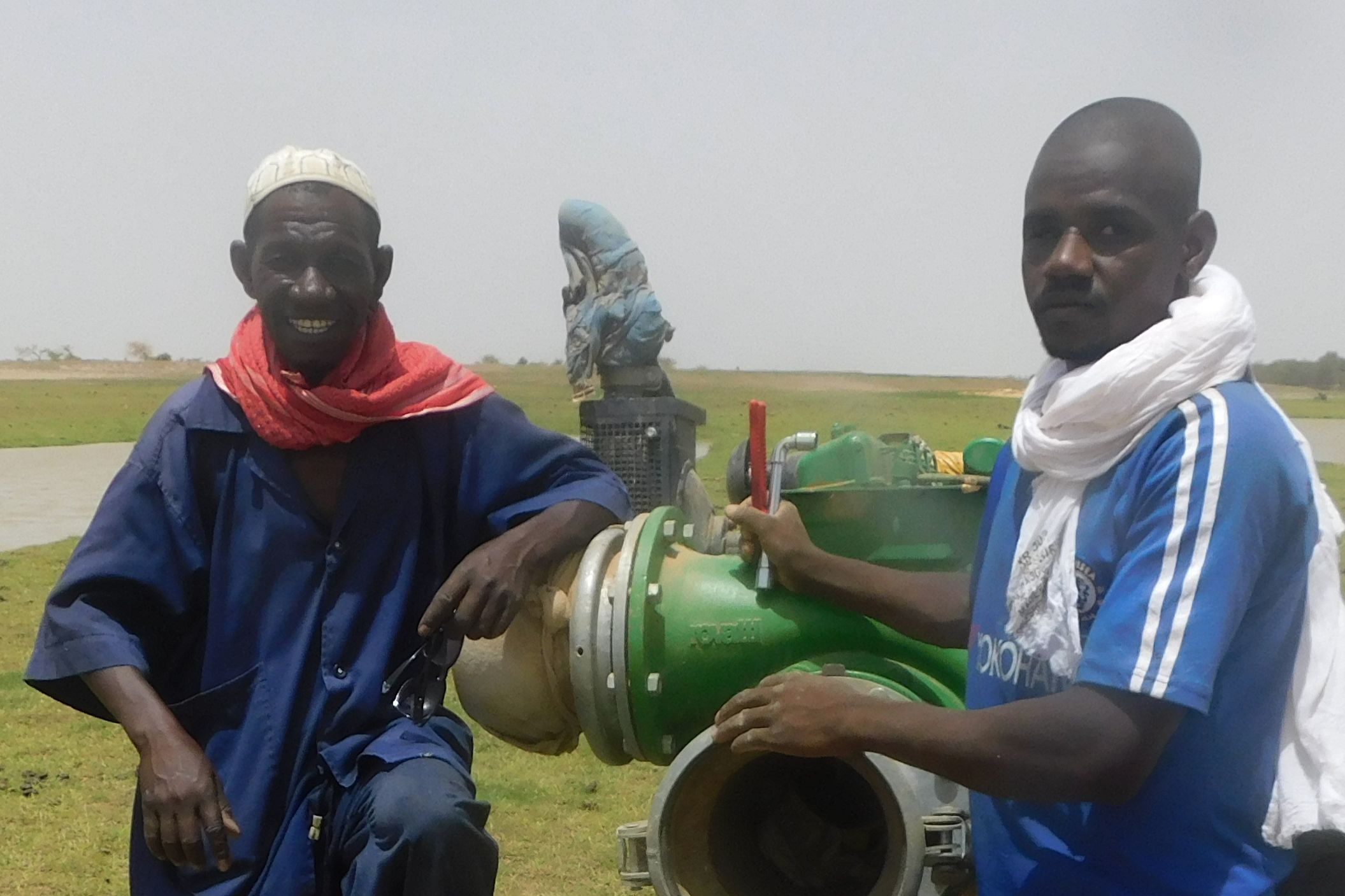 Szene auf dem Reisfeld mit zwei Männern, in ihrer Mitte Rohre und Ventile einer großen Pumpanlage