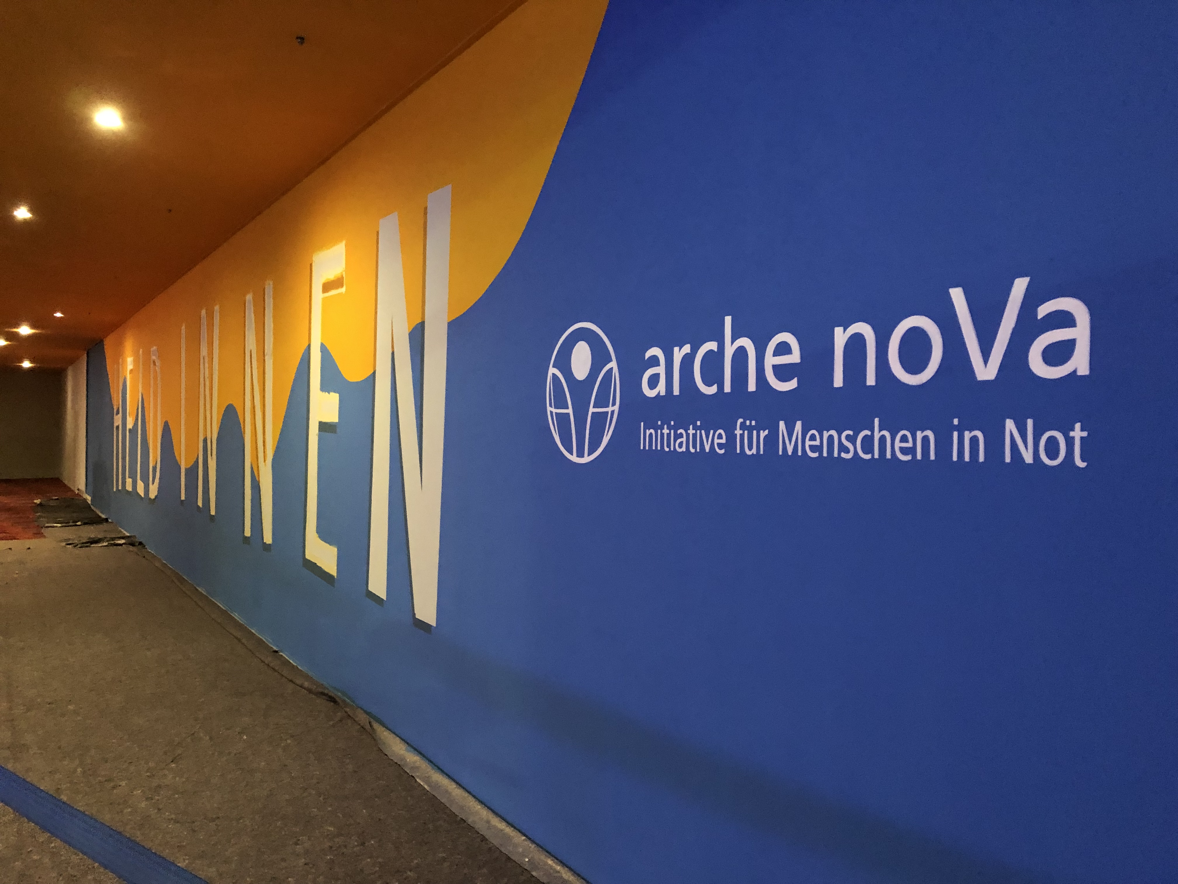 der Schriftzug arche noVa steht auf blauem Grund auf einer Wand, daneben ein Schriftzug auf blau-gelbem Wellengrund