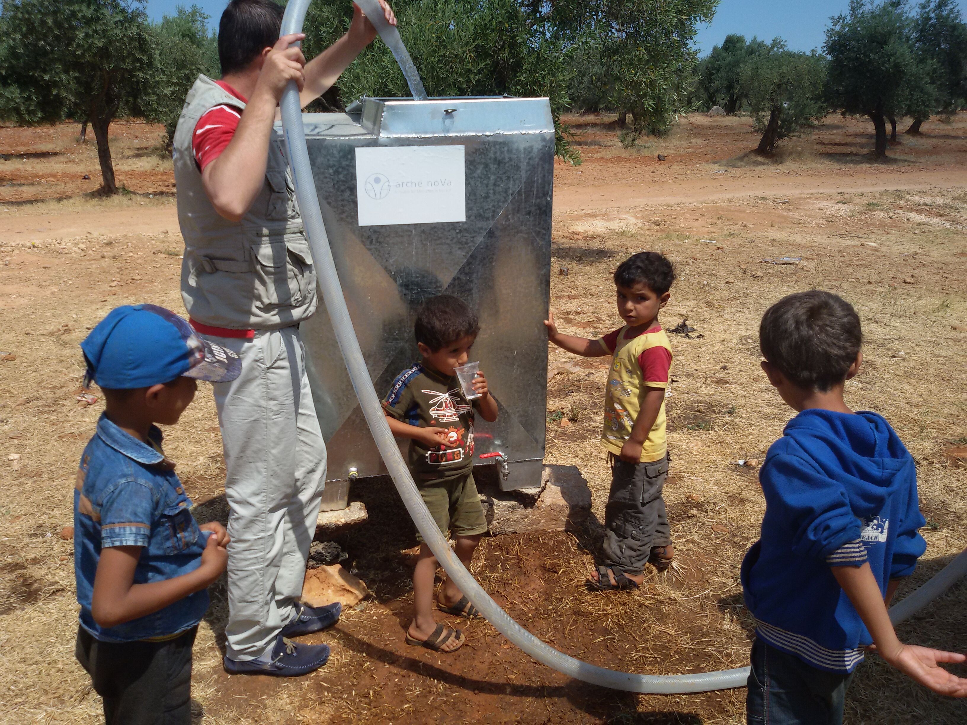 ein Mann füllt einen Wassertank, Kinder stehen daneben