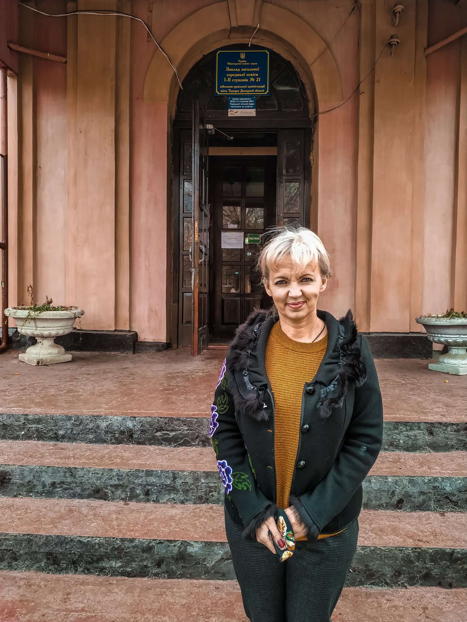 eine Frau, Lilija Filenko, Schuldirektorin, steht vor einem Eingang
