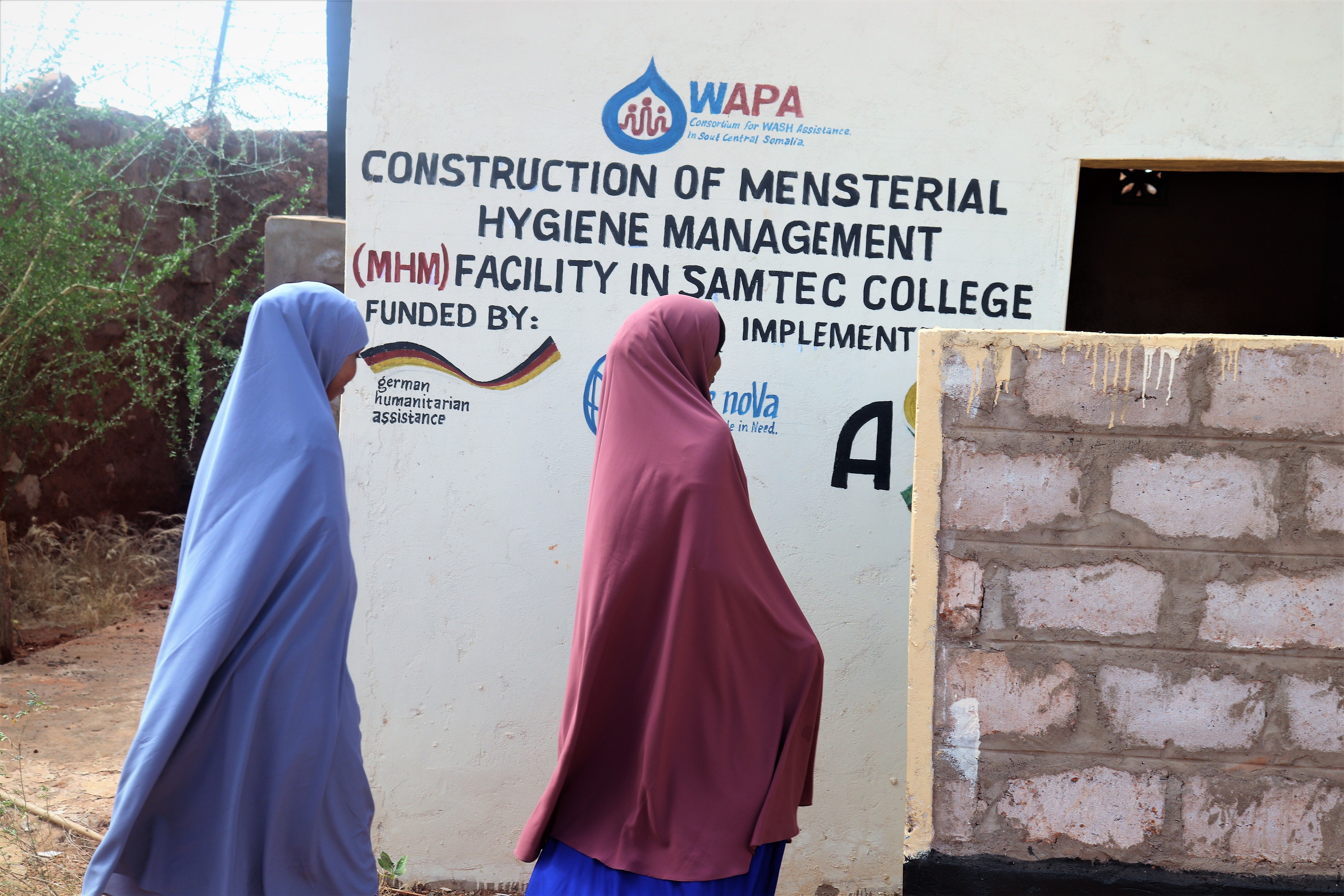 Mädchen laufen zur neuen Toilette vor einem Schild mit den Projektpartnern