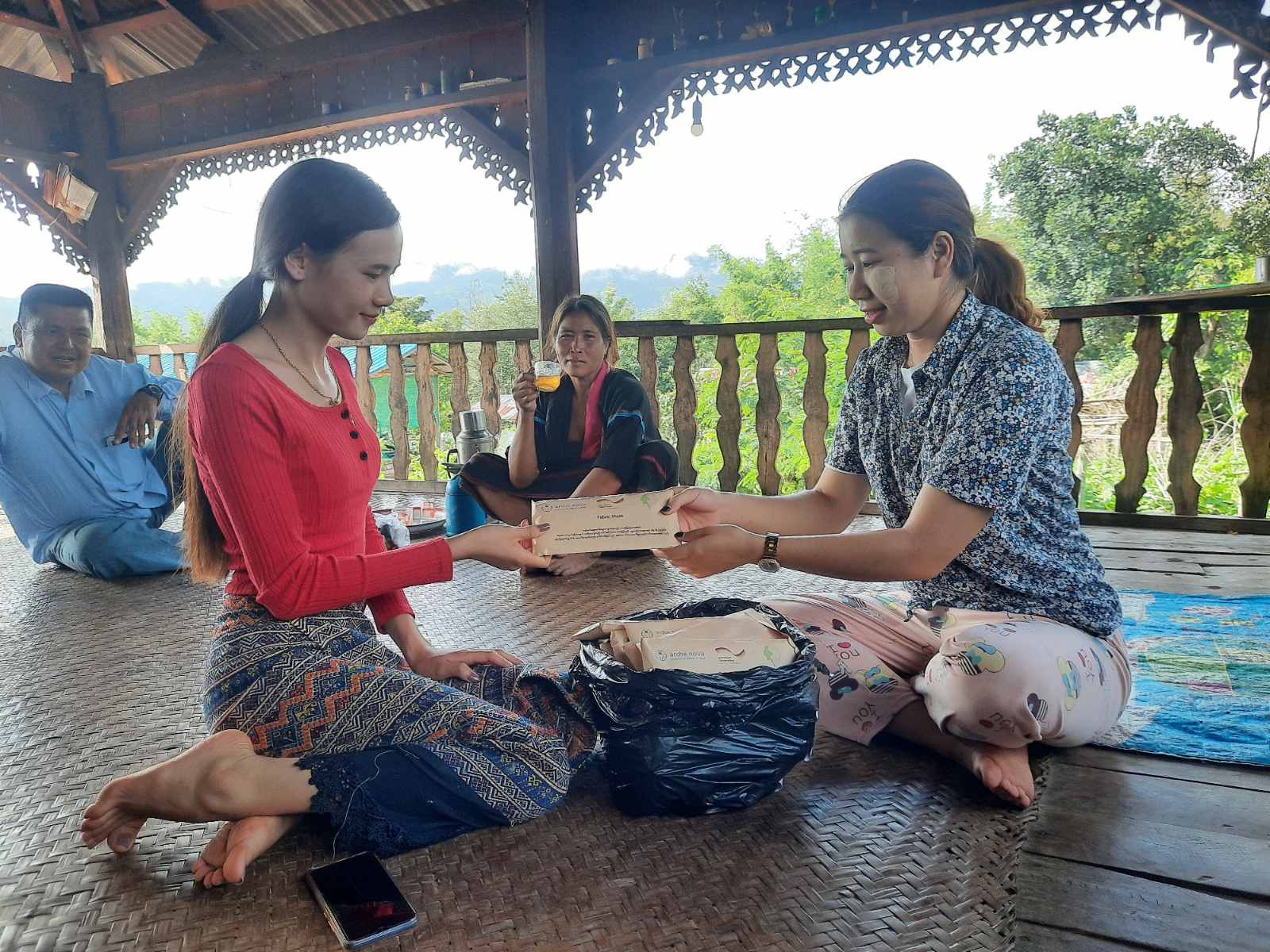 Zwei myanmarische Frauen sitzen auf dem Boden und halten zwischen sich eine Geschichtsmaske