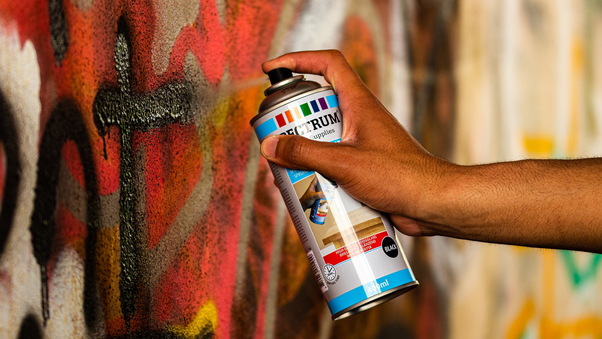 Hand hat Spraydose in der Hand und besprüht Wand mit Graffiti