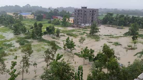 Luftbild von überschwemmten Feldern, einzelne Bäume ragen aus dem Wasser, im Hintergrund ein Gebäude 