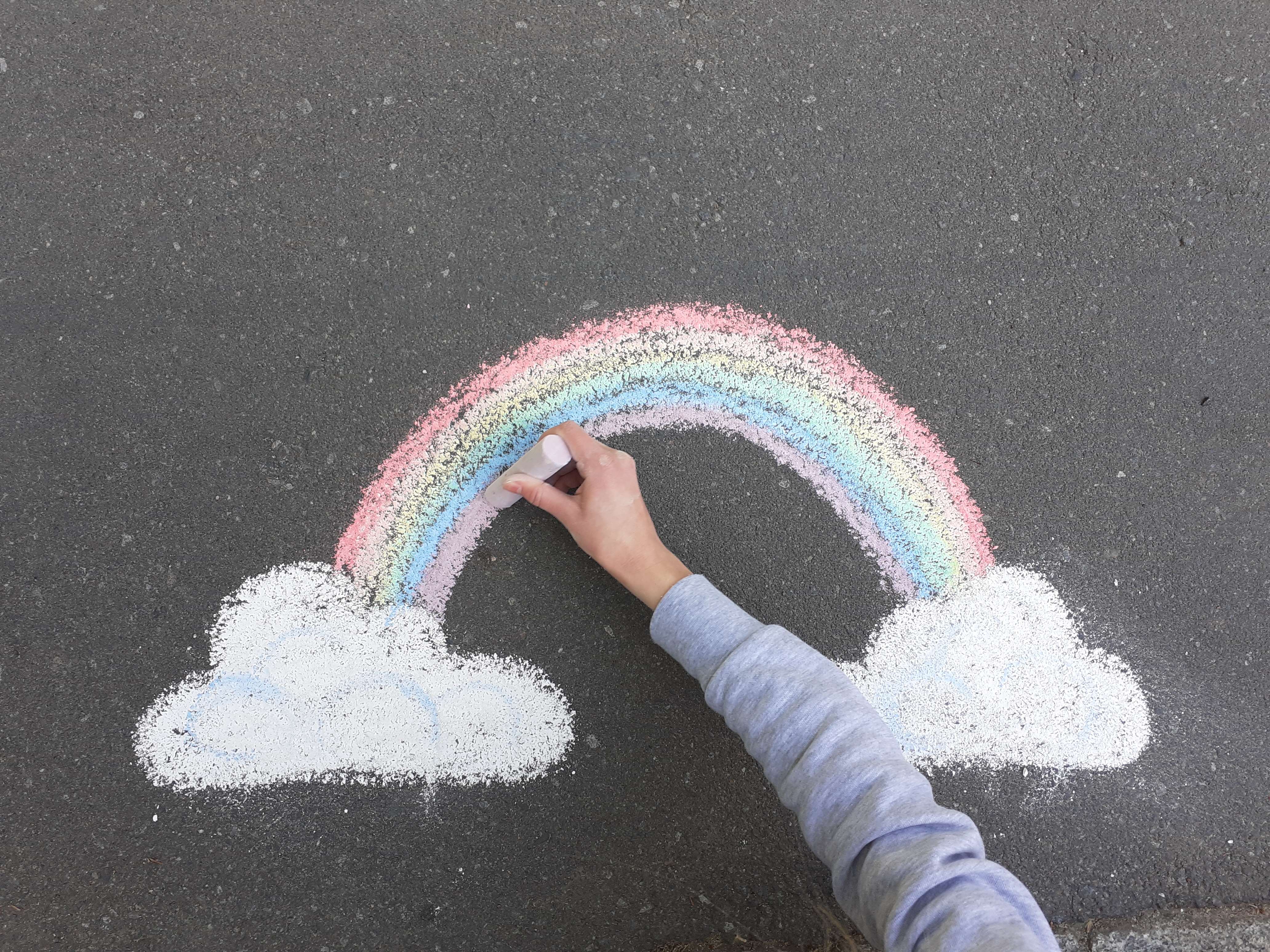 ein Kind malt einen Regenbogen auf die Straße