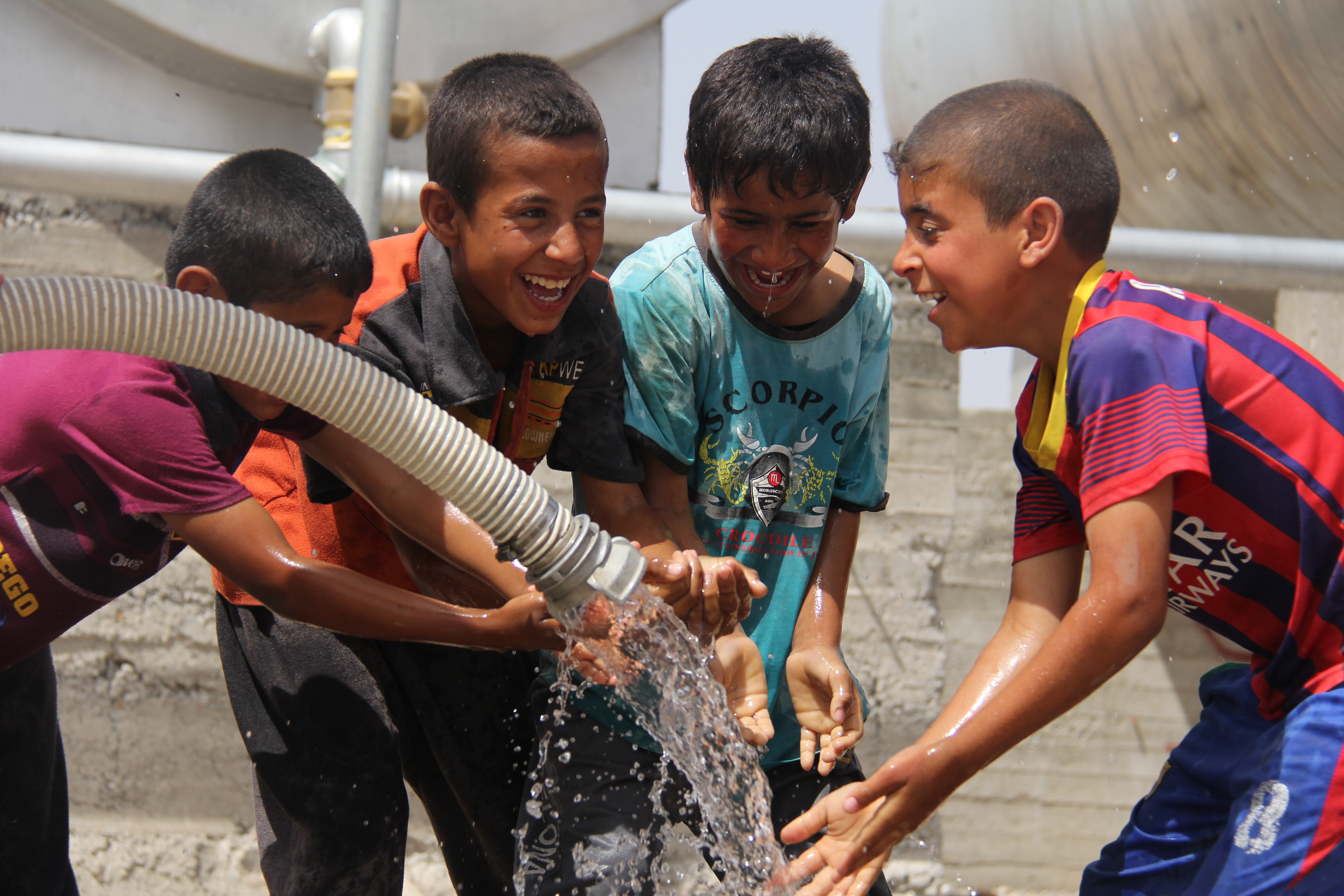 Vier irakische Jungen freuen sich über das saubere Wasser, das aus der Leitung sprudelt