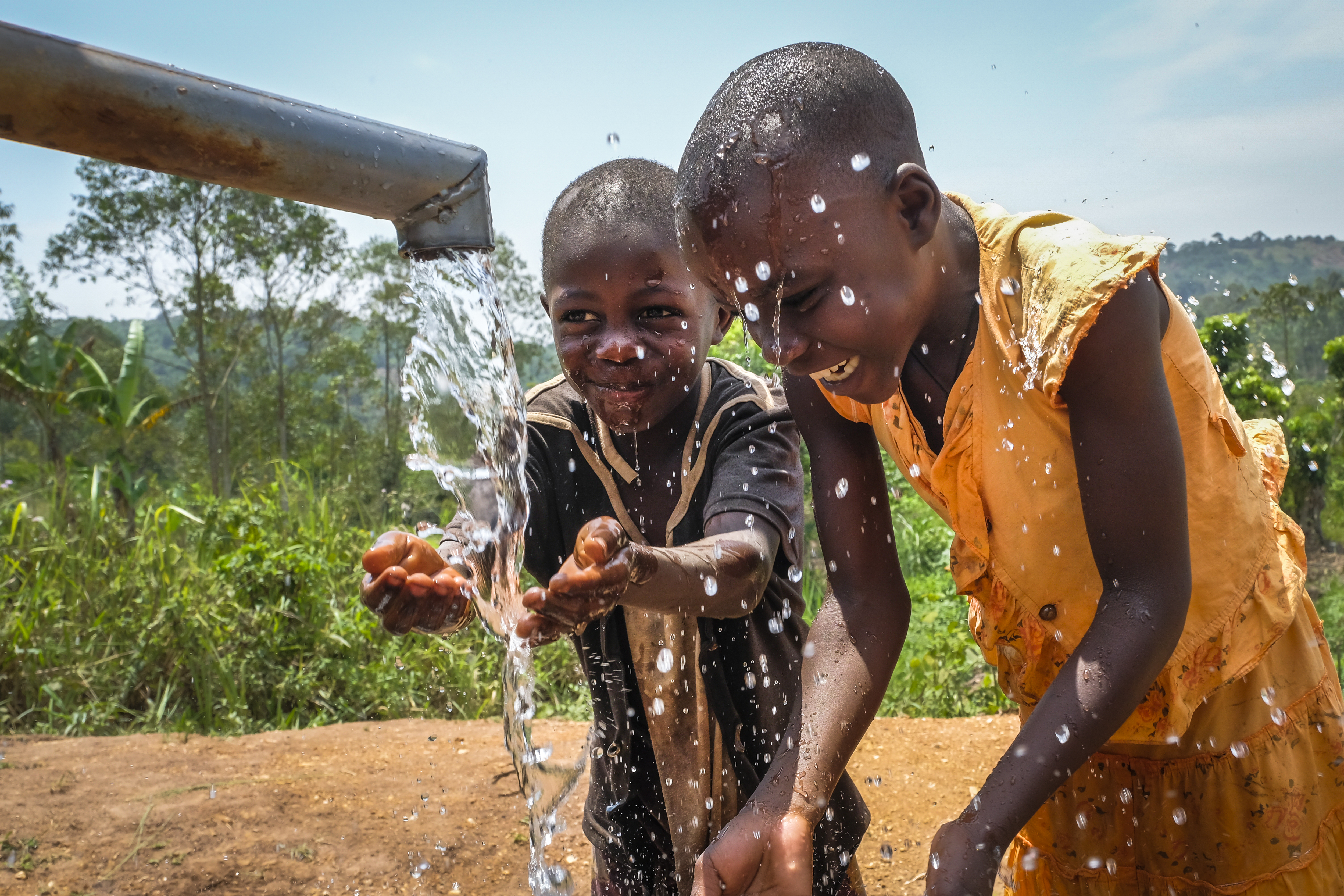 Zwei Kinder freuen sich über Wasser aus einer Brunnenhandpumpe