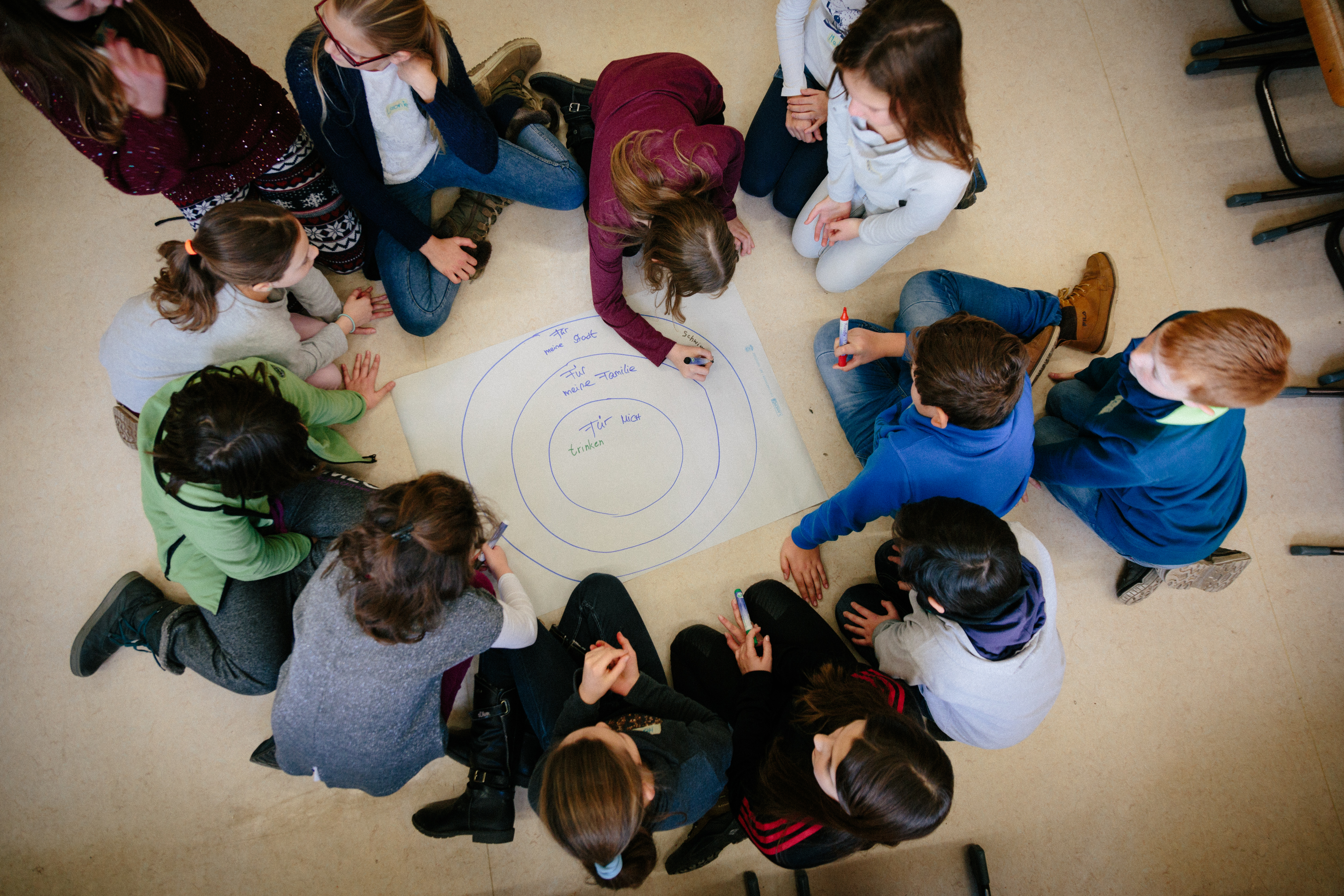 Kinder sitzen auf dem Boden im Kreis um einen großen beschrieben Papierbogen