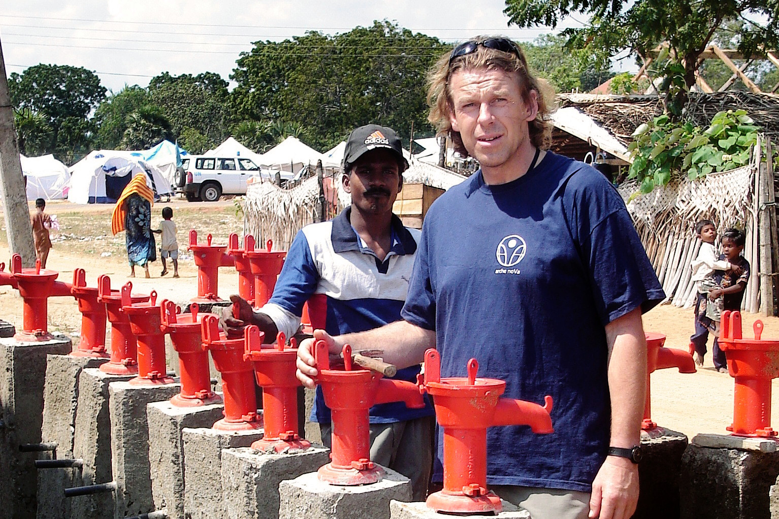 Zwei Männer an einer Reihe roter Brunnenpumpen ohne Handschwengel