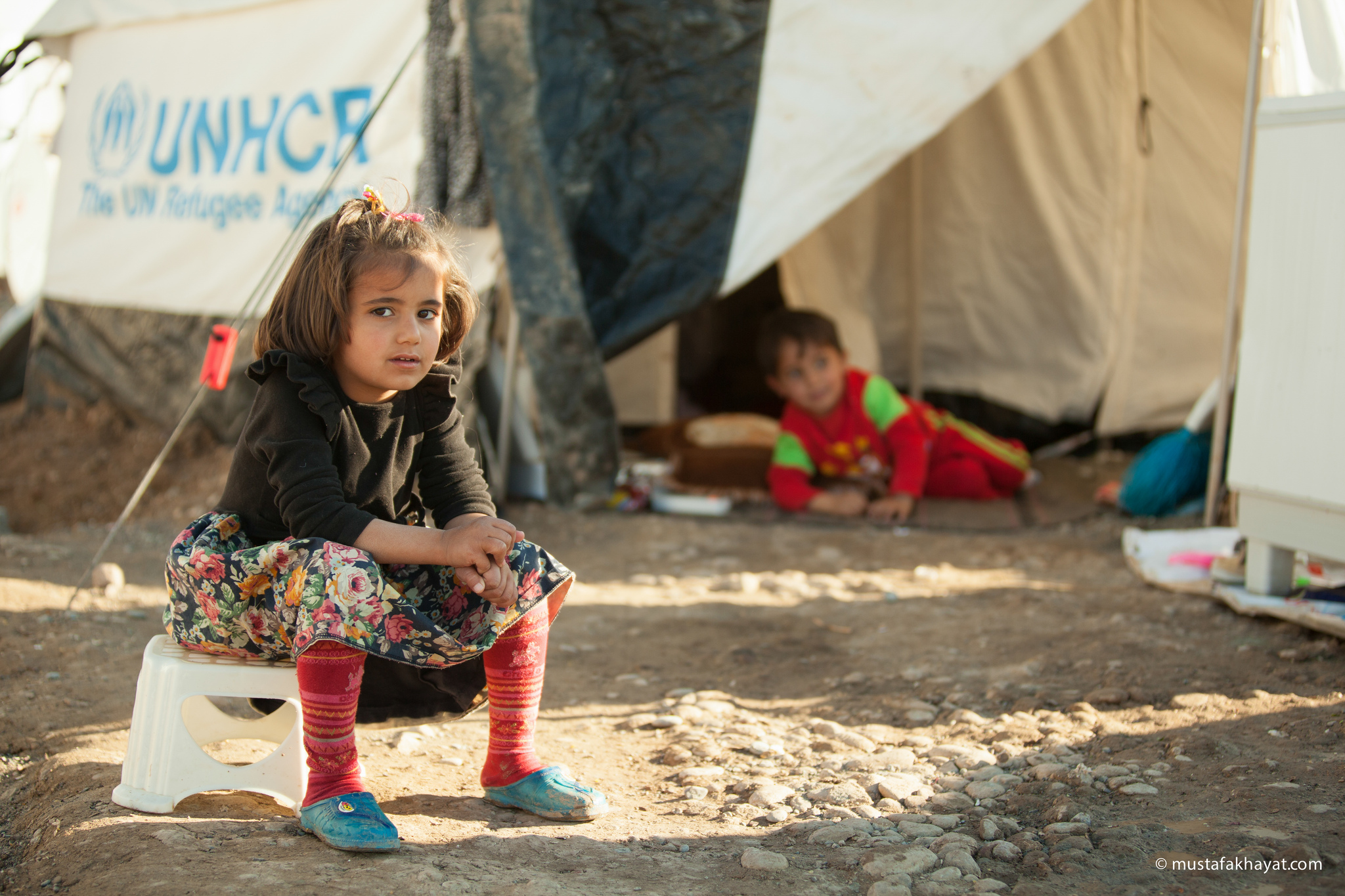 Mädchen in einem Flüchtlingsheim sitzt vor ihrem Zelt