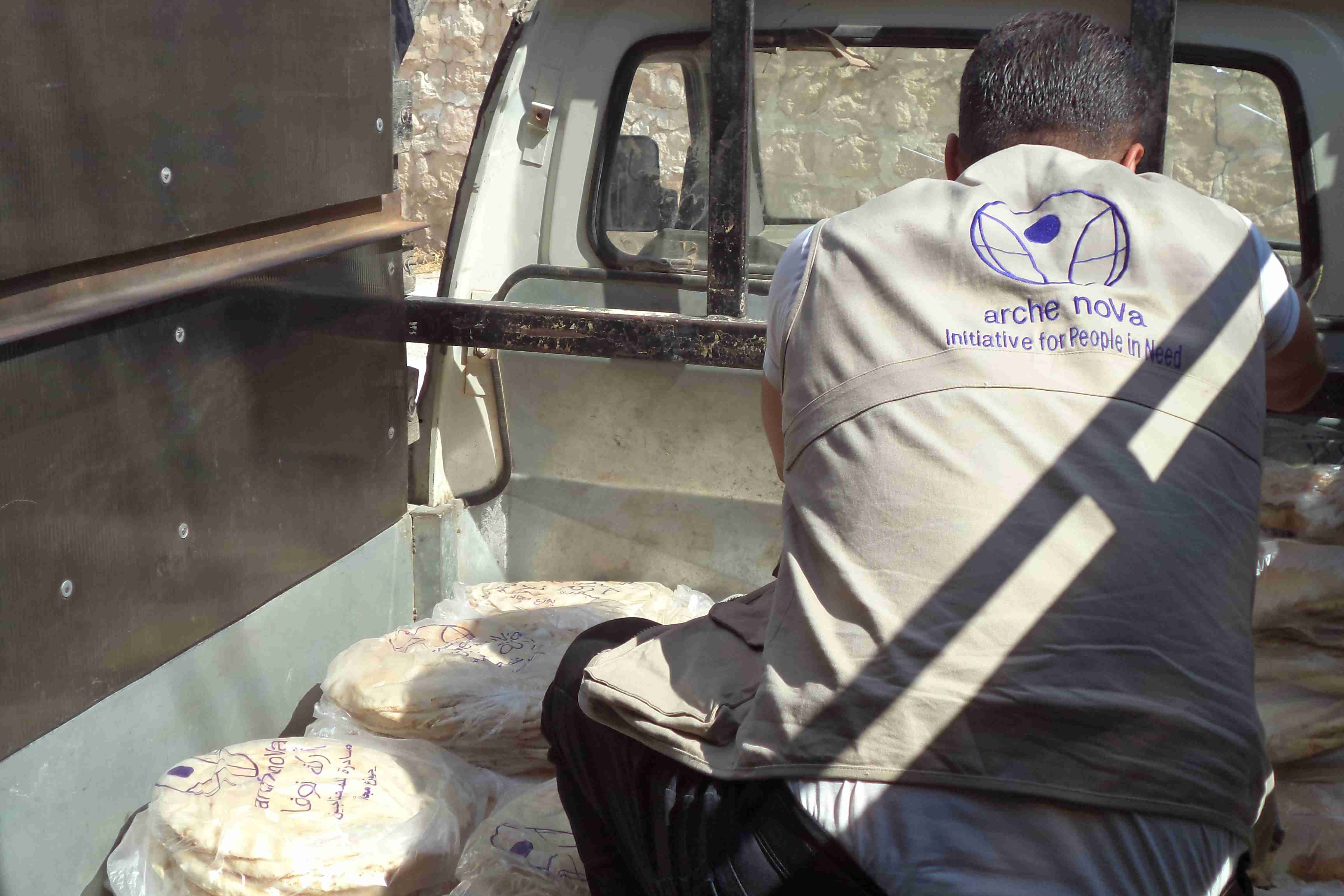 ein arche noVa Mitarbeiter verstaut Brotpakete auf der Ladefläche eines Transporters