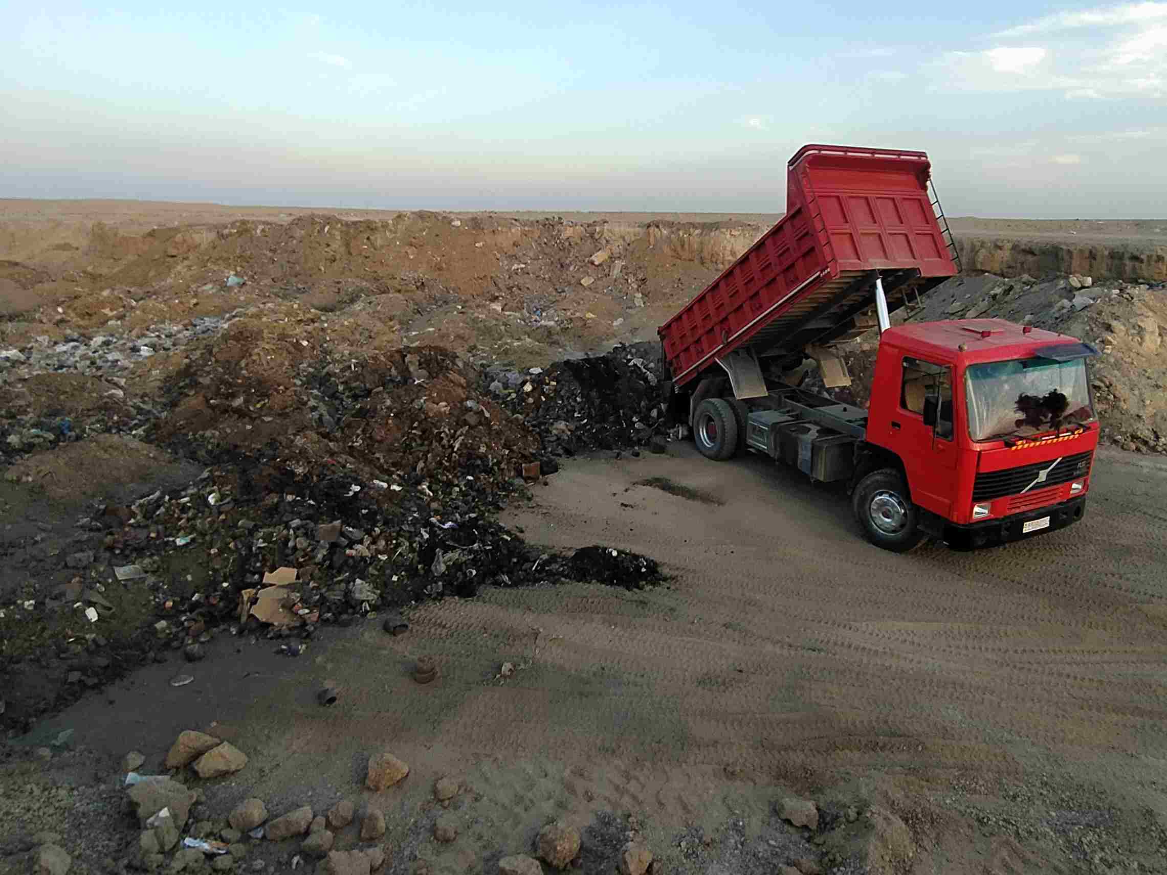 Roter Kipplader entleert Ladung an Mülldeponie vor offener Landschaft