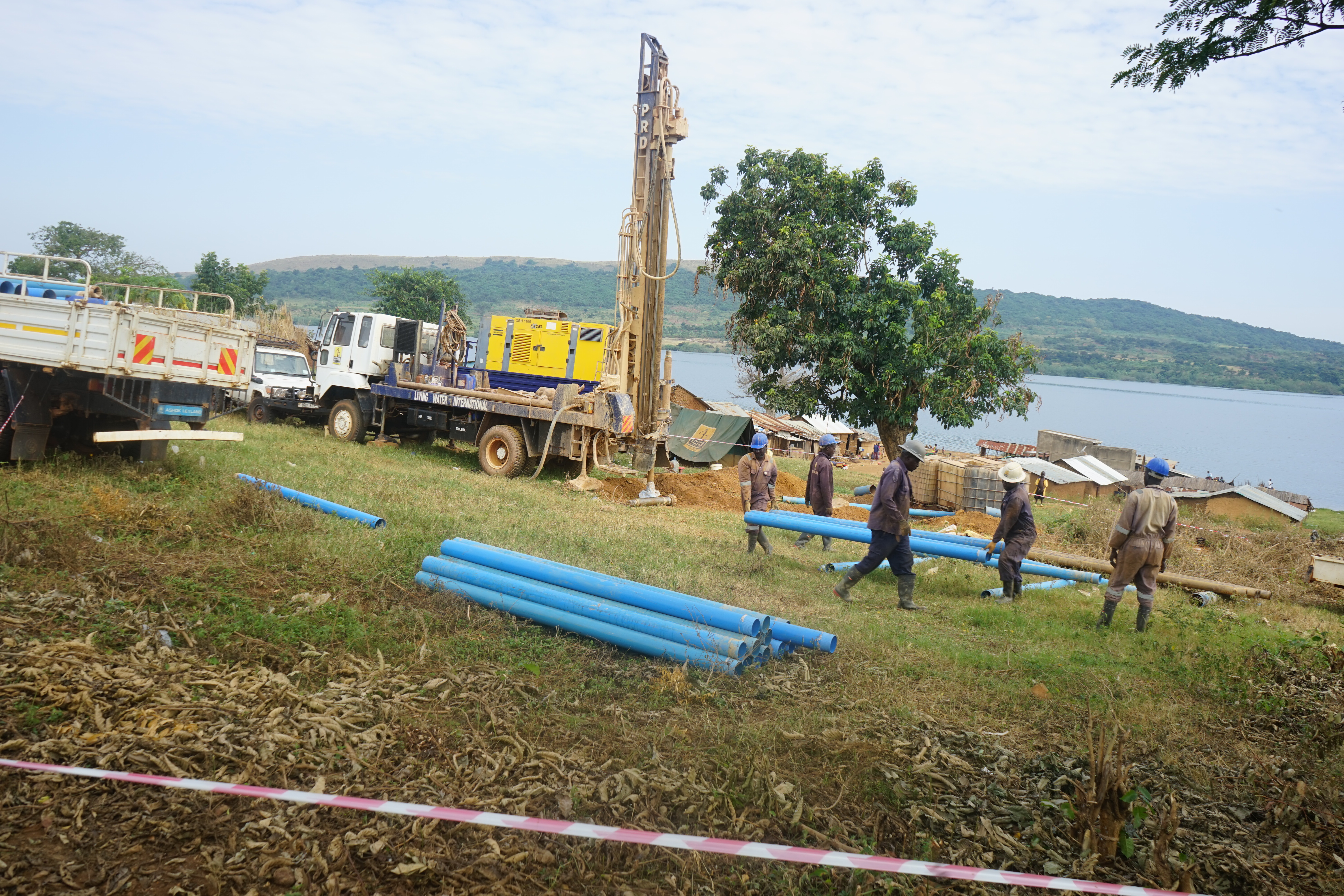 Blaue Rohre liegen auf einer Wiese, im Hintergrund ein LKW mit Bohrkonstruktion auf der Heckfläche und der Viktoriasee