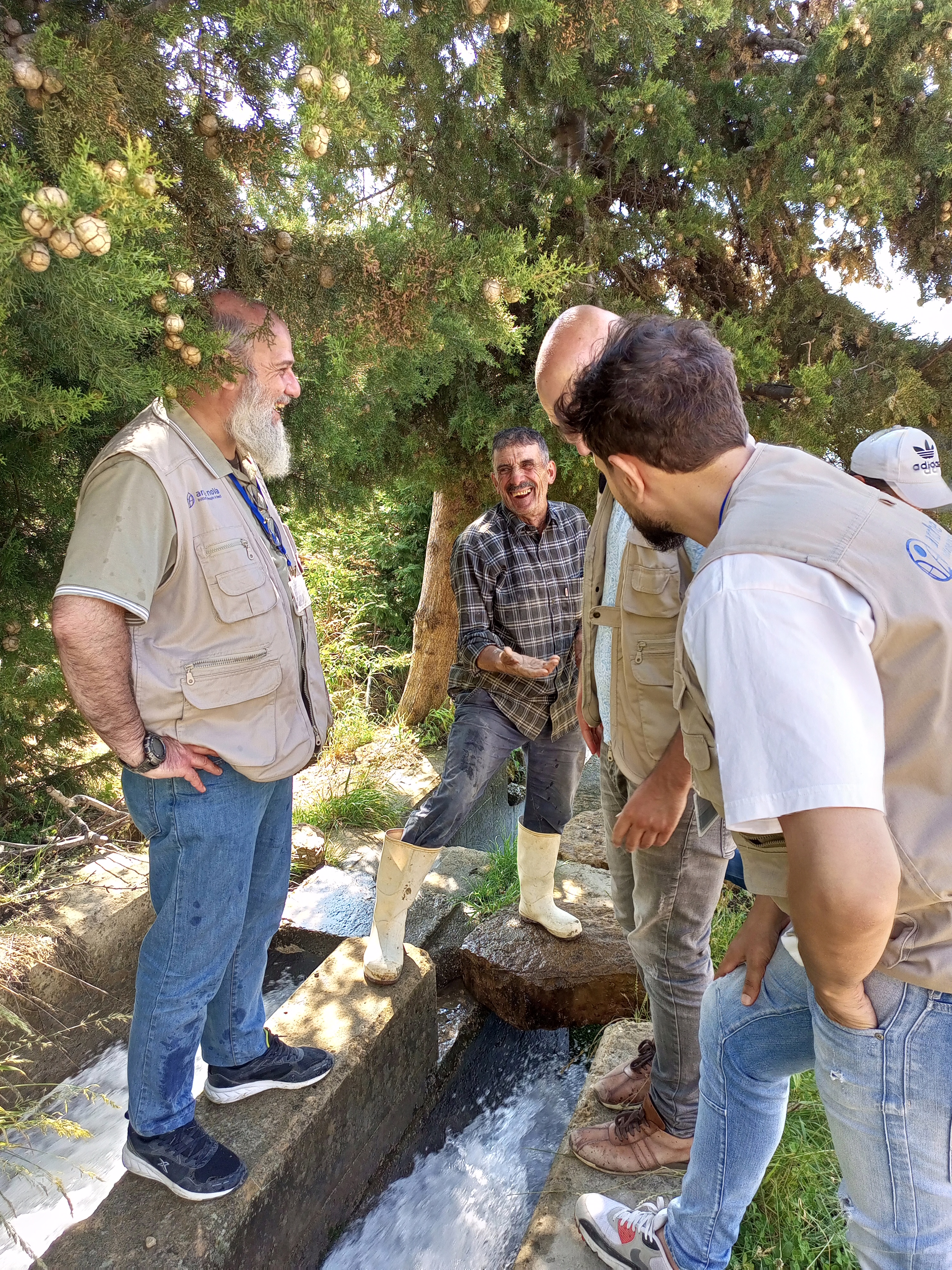 Vier Männer an einem Bewässerungskanal, einer blickt lachend Richtung Kamera
