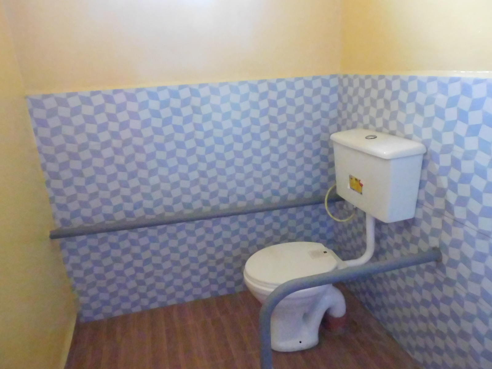 Ein Toilettensitz mit Spülkasten im Halbprofil fotografiert, rechts und links Griffe