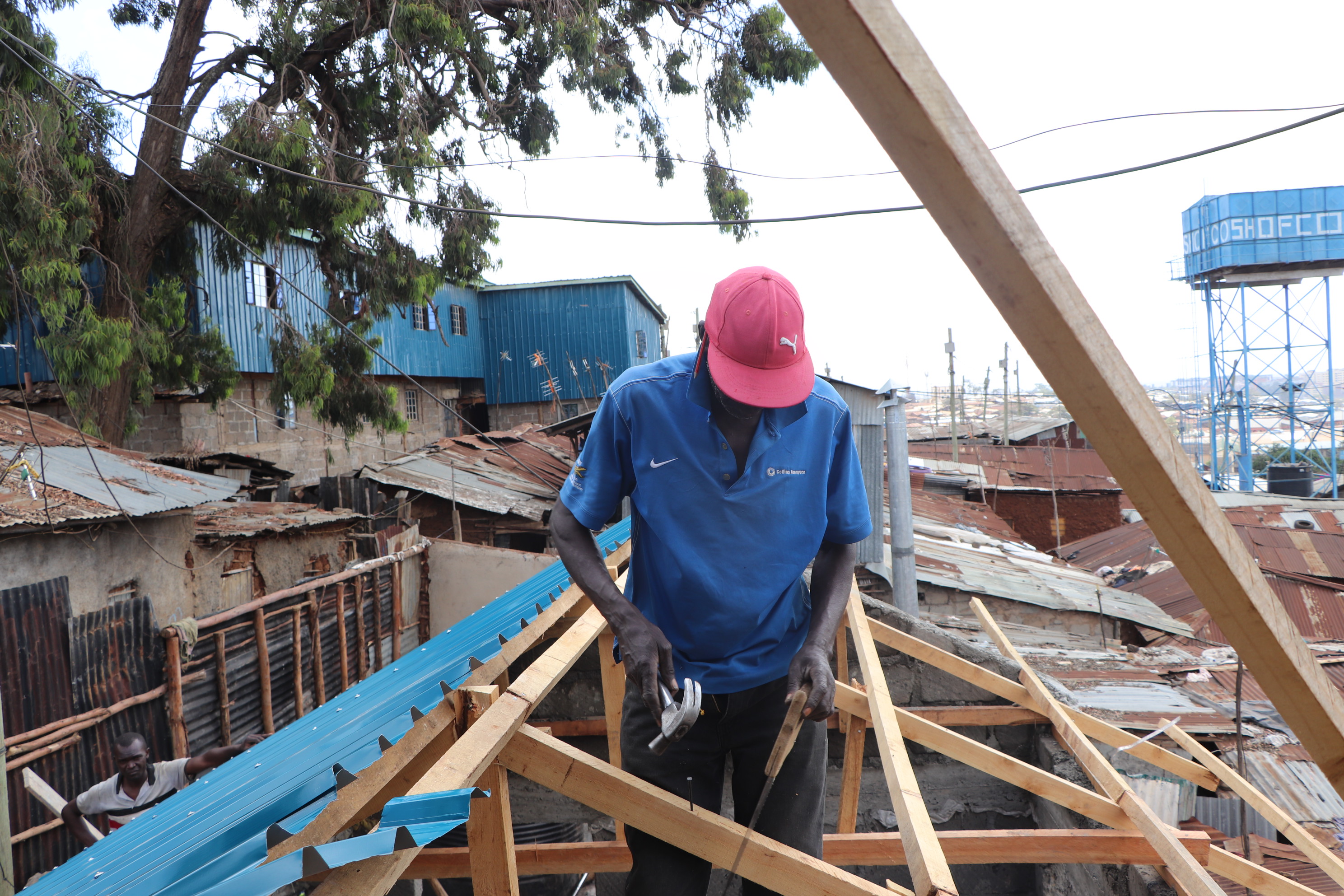 Ein Bauarbeiter arbeitet mit einem Werkzeug an Latten in einem schon halb gedeckten Dachstuhl