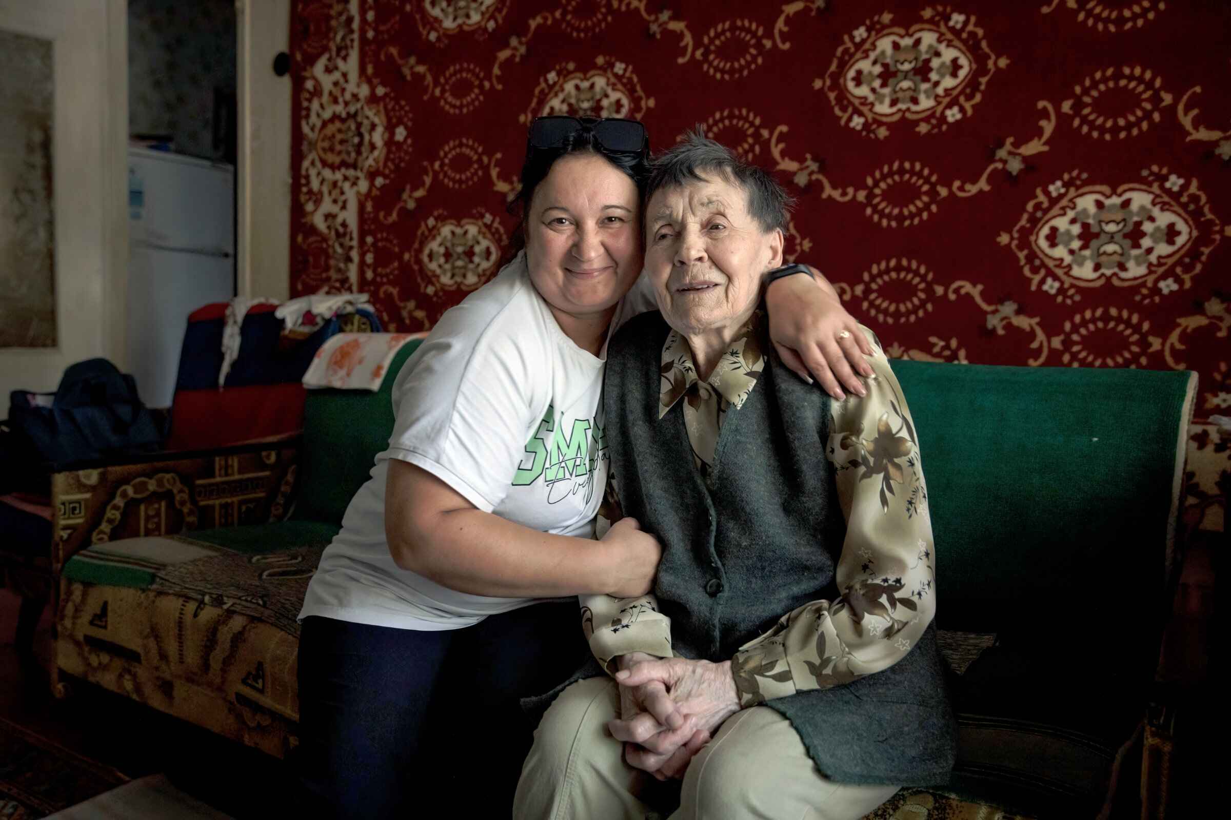 Eine jüngere und eine ältere Frau auf einem grünen Sofa vor roter Ornamenttapete