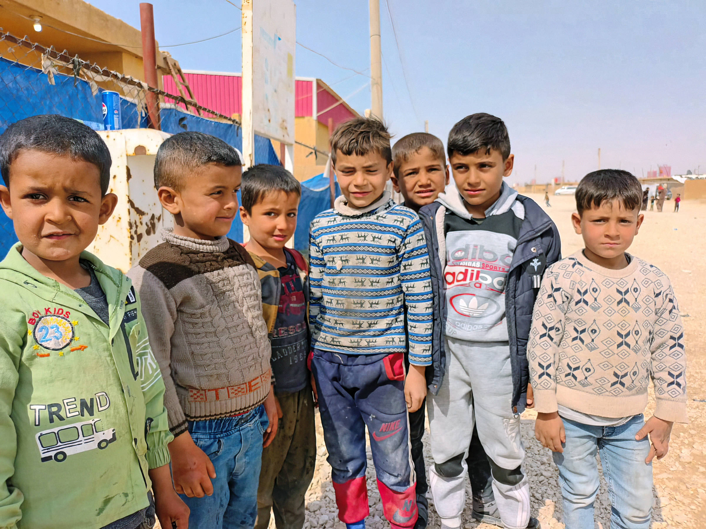 Eine Gruppe von Jungen schaut in die Kamera. Im Hintergrund sind Gebäude und eine staubige Strasse zu sehen.