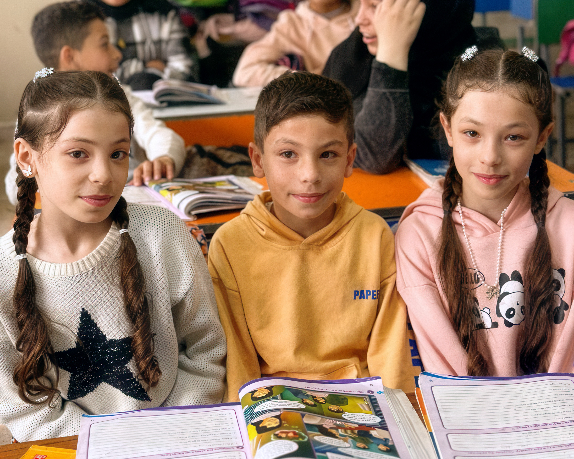 Drei Kinder vor aufgeschlagenen Schulheften.