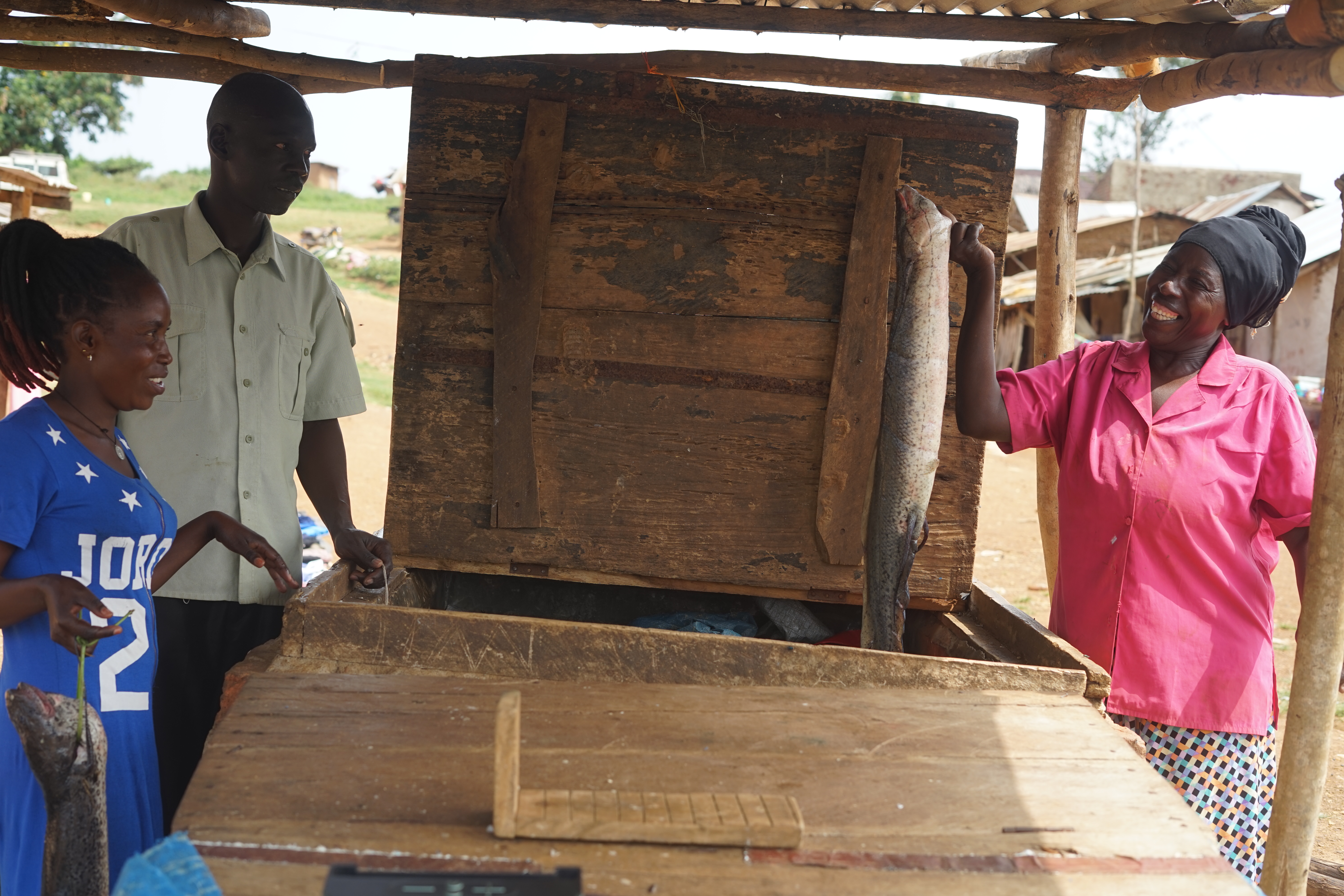 Eine Frau rechts im Bild hält lachend einen großen Fisch, links beobachten sie dabei ein Mann und eine Frau