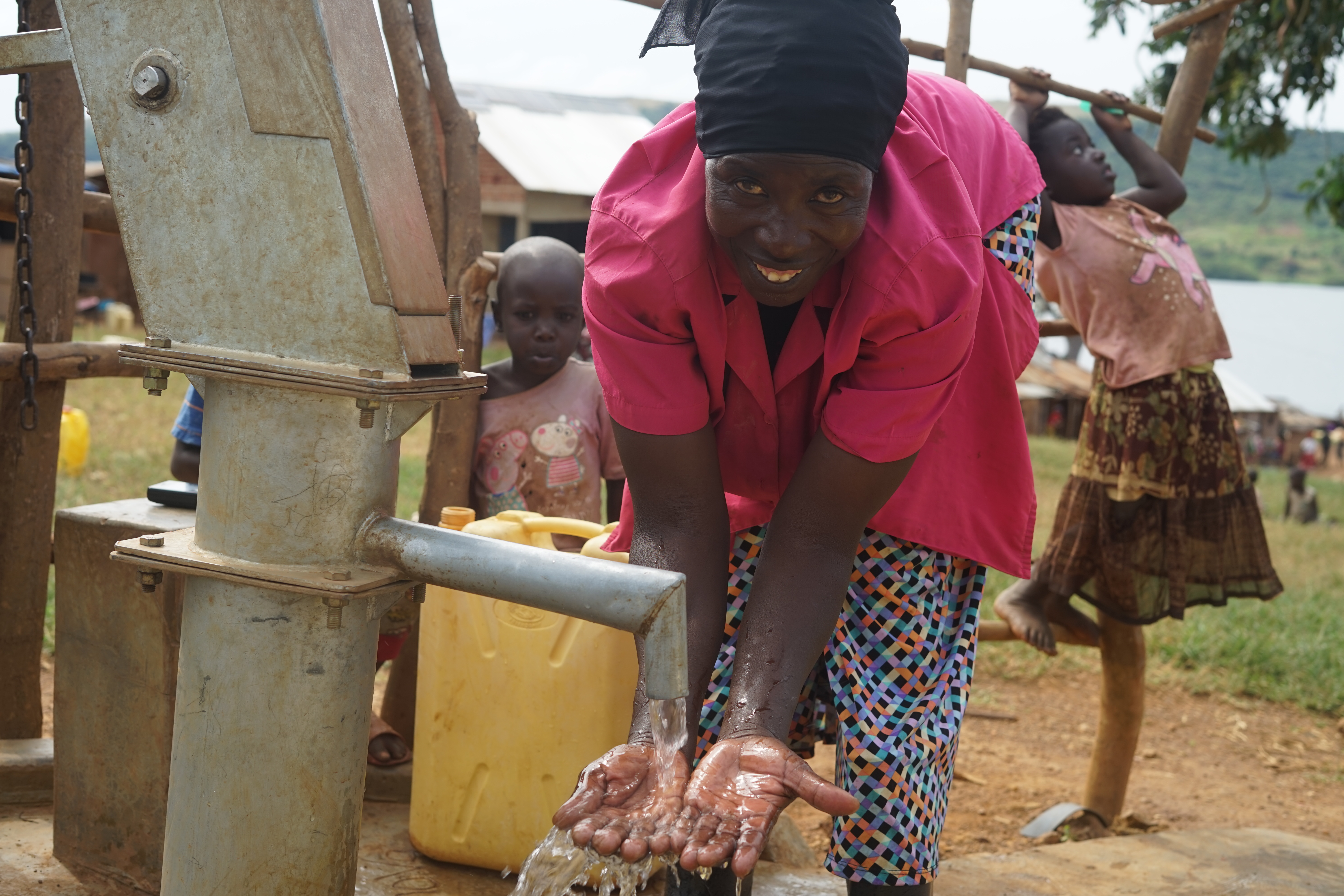 Frau an einer Handpumpe, sie schaut lächelnd in die Kamera