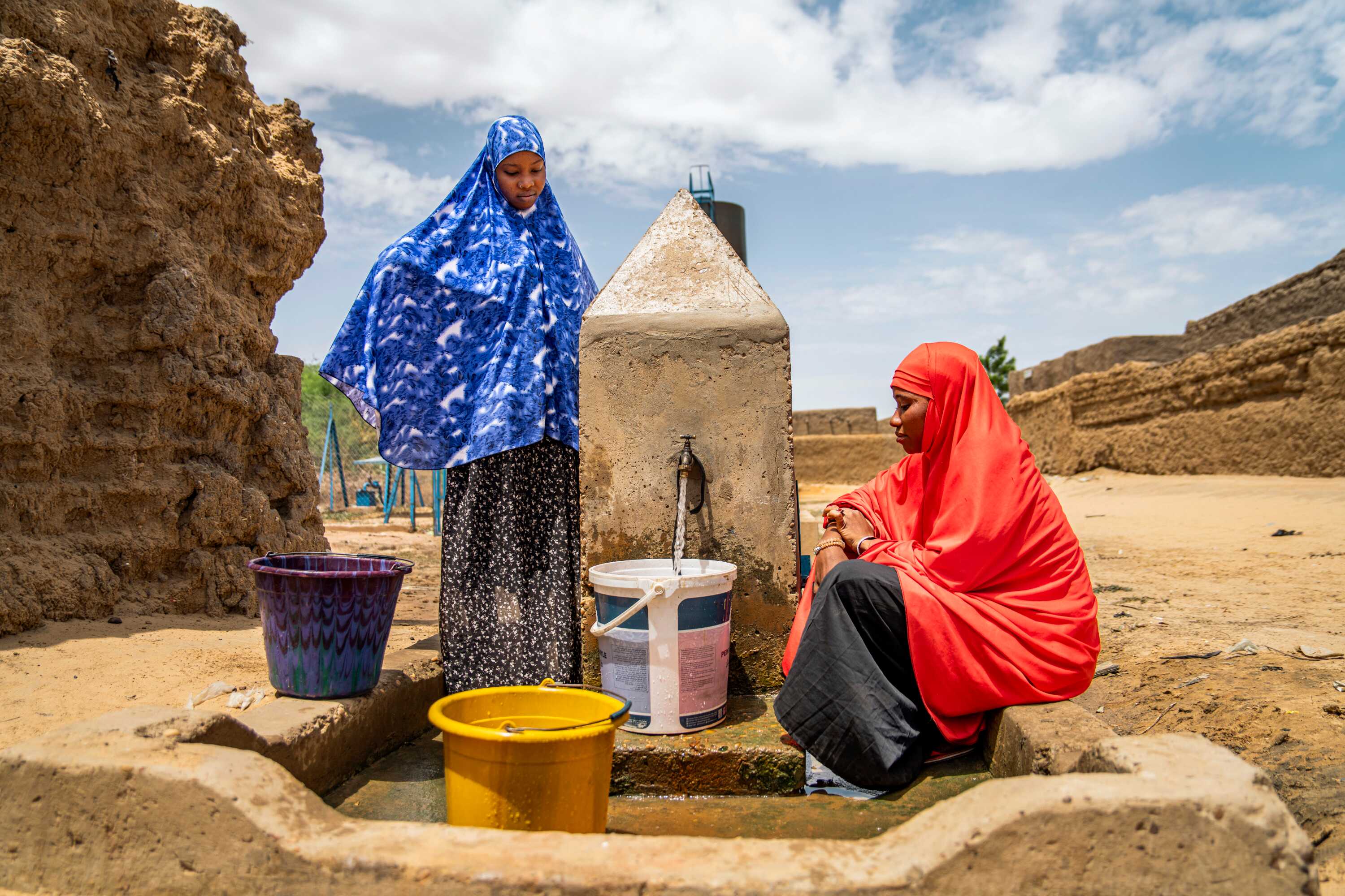 Zwei Frauen befüllen an einem Brunnen Eimer mit Wasser