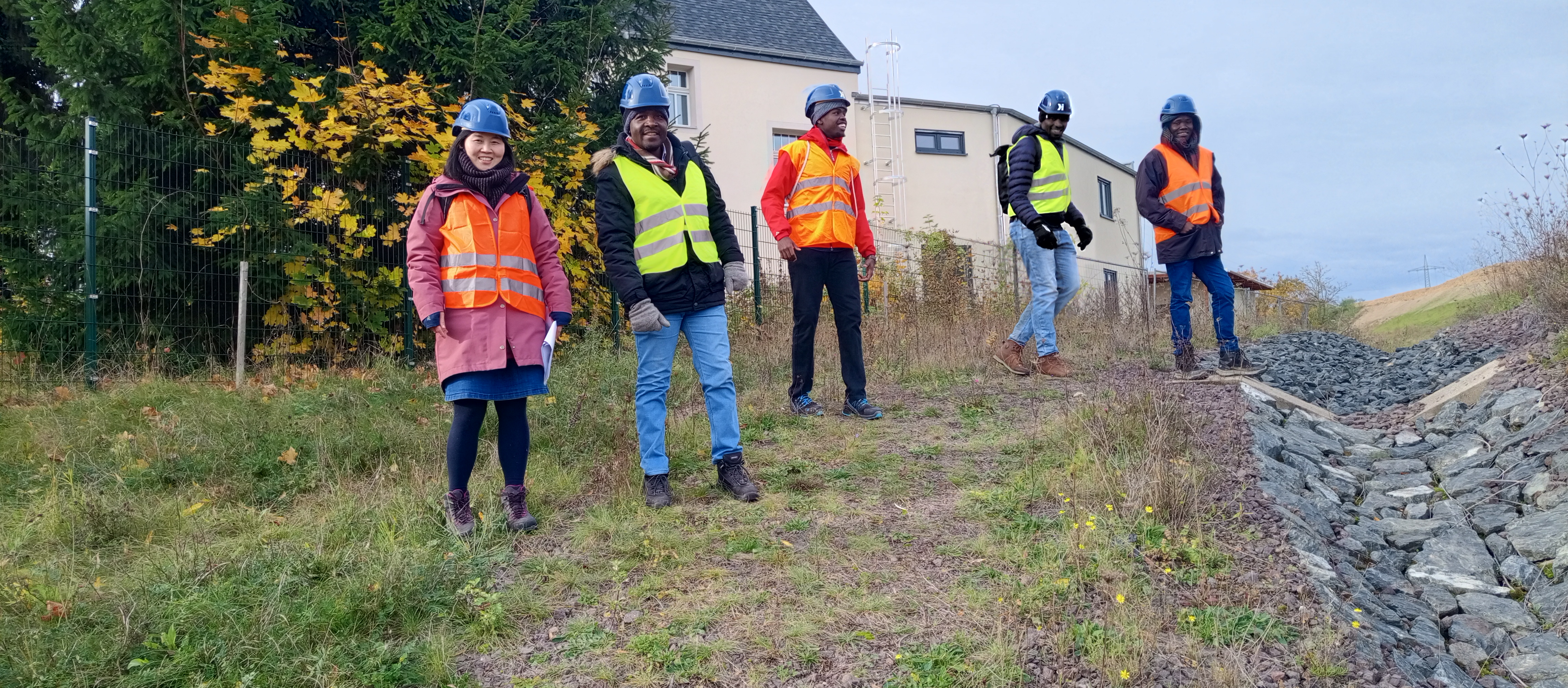 Vier Personen stehen auf einer Wiese, sie tragen Helme und Signalwesten.