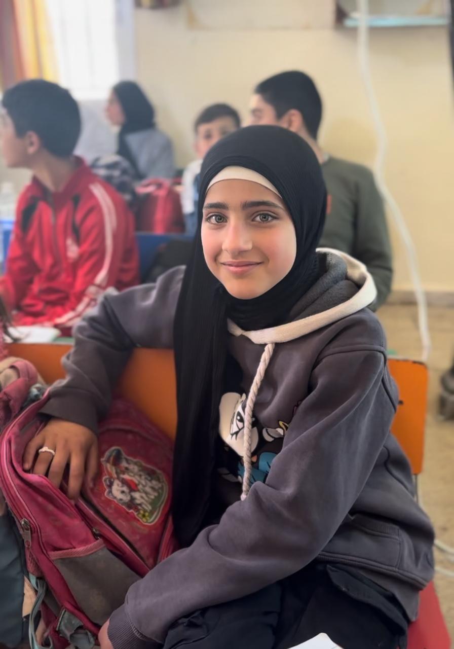 Ein ungefähr 10 Jahre altes Mädchen sitzt im Klassenzimmer, neben ihr liegt ein Schulrucksack