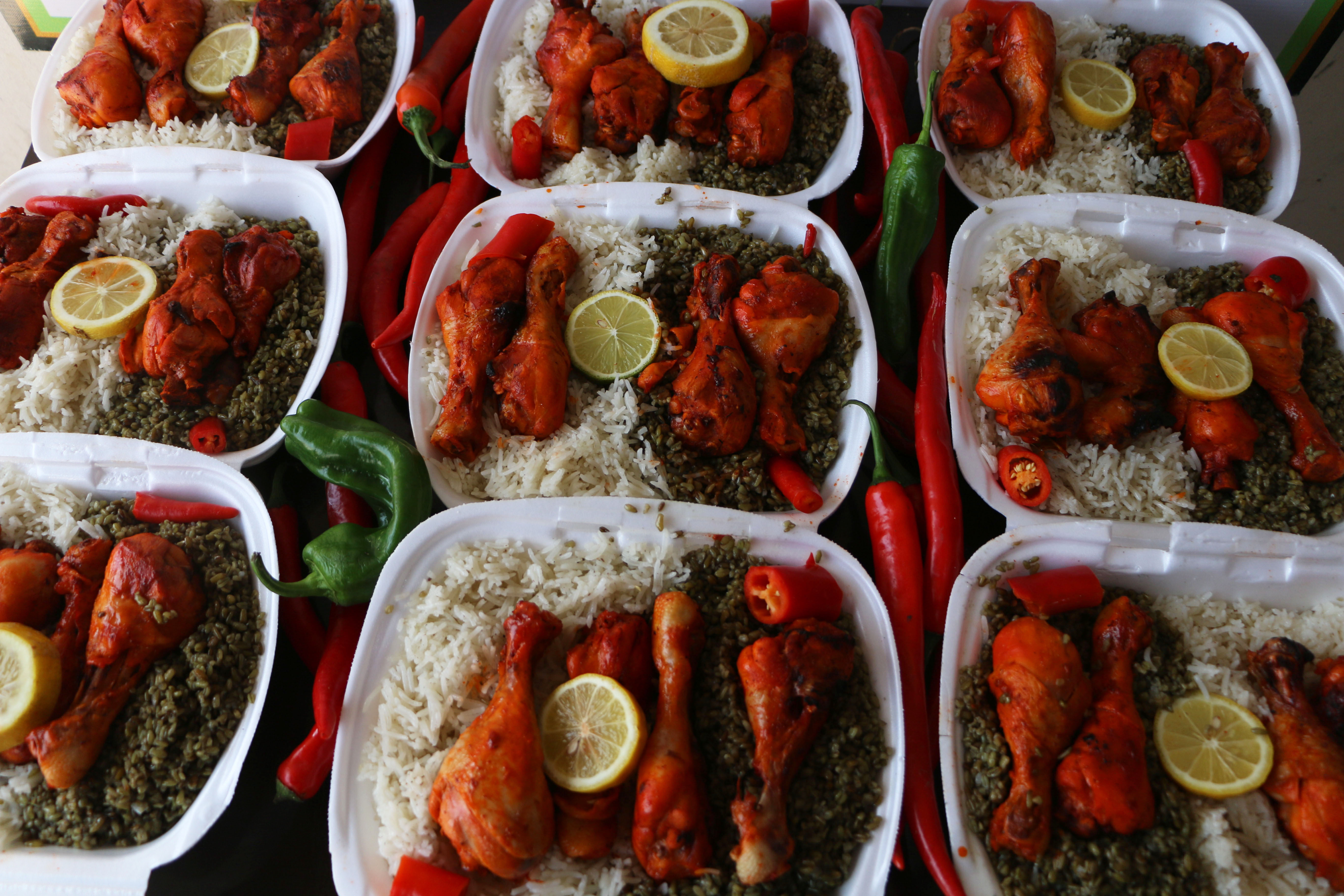 Aus der Vogelperspektive Blick auf rund 10 Kunststoffassietten gefüllt mit Reis Hähnchenkeule Gemüse und Zitronenscheibe