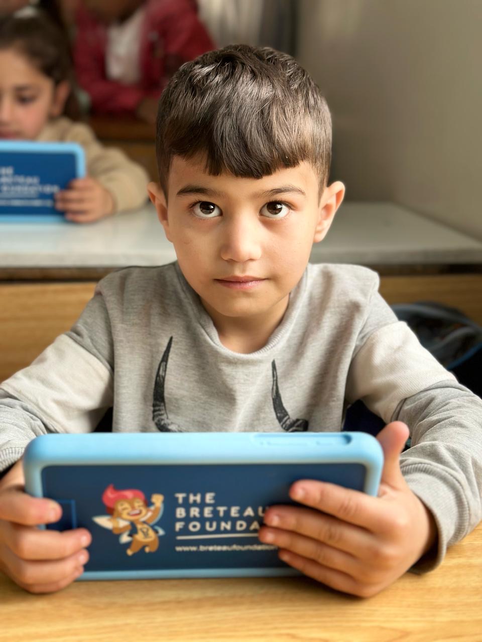 Ein ungefähr 6 Jahre alter Junge sitzt im Klassenzimmer und schaut schüchtern in die Kamera