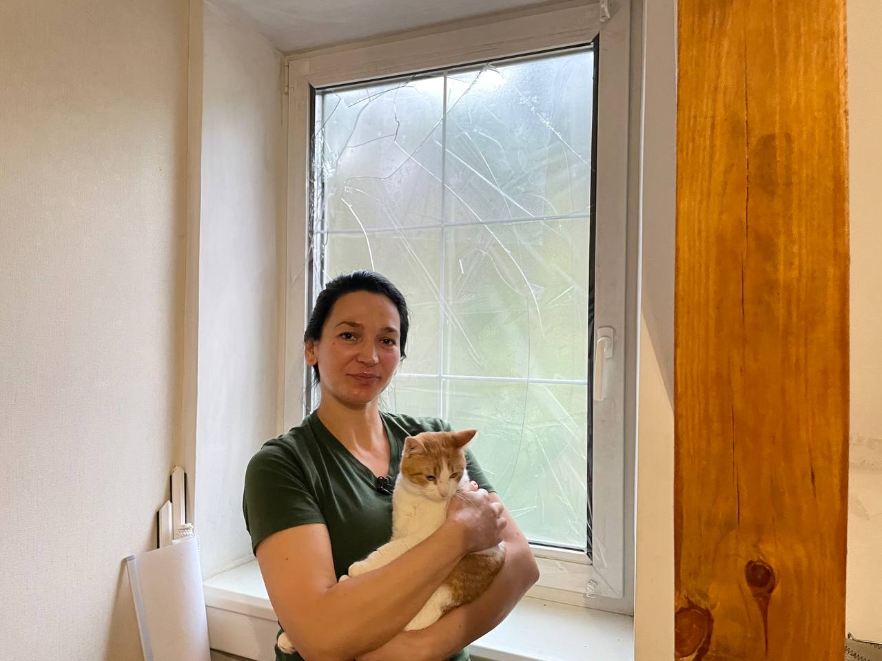 Frau mit Katze auf dem Arm steht vor einem Fenster