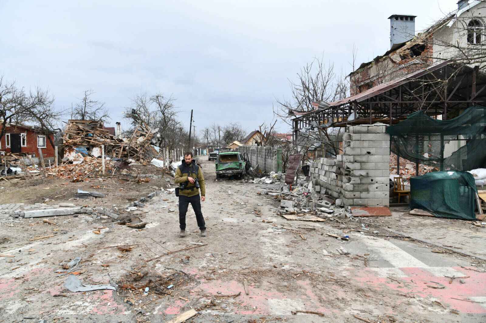 A man in a street with completely destroyed houses and vehicles