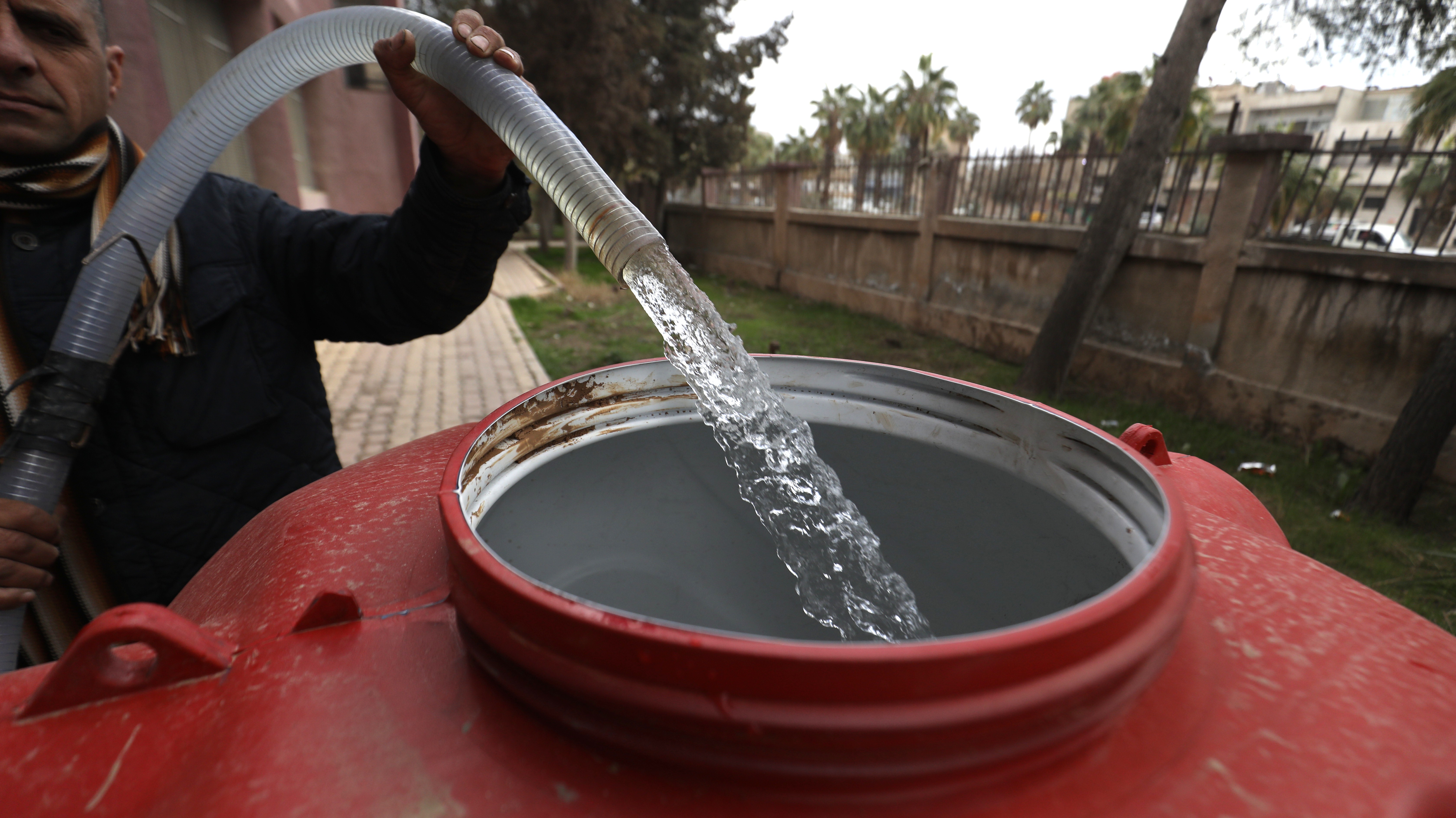 Wasserstrahl fließt aus einem Schlauch in die Öffnung eines großen, roten Wassertanks