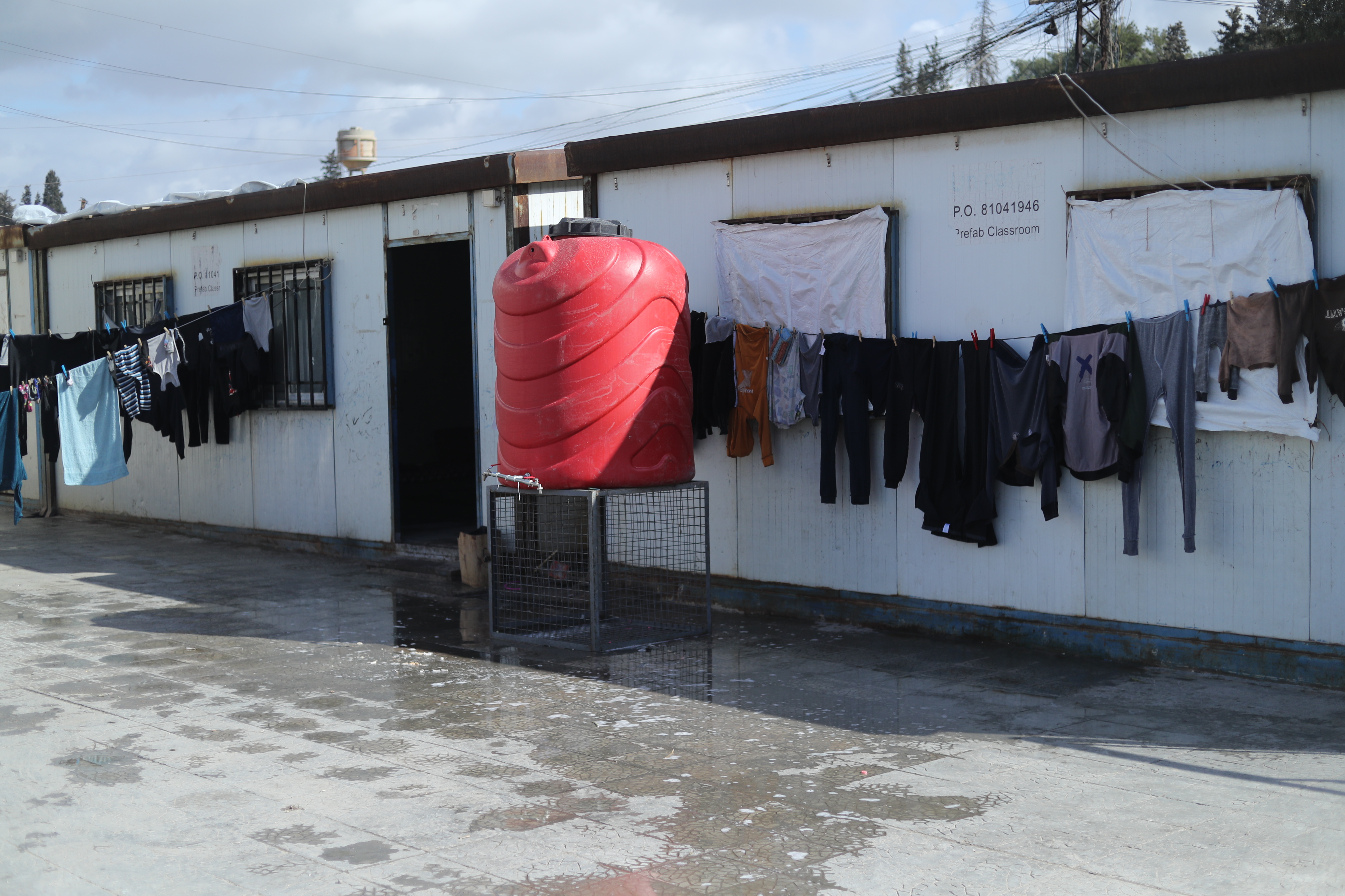 Kleines, flaches Gebäude, davor ein roter Wassertank und eine Leine voller Wäsche