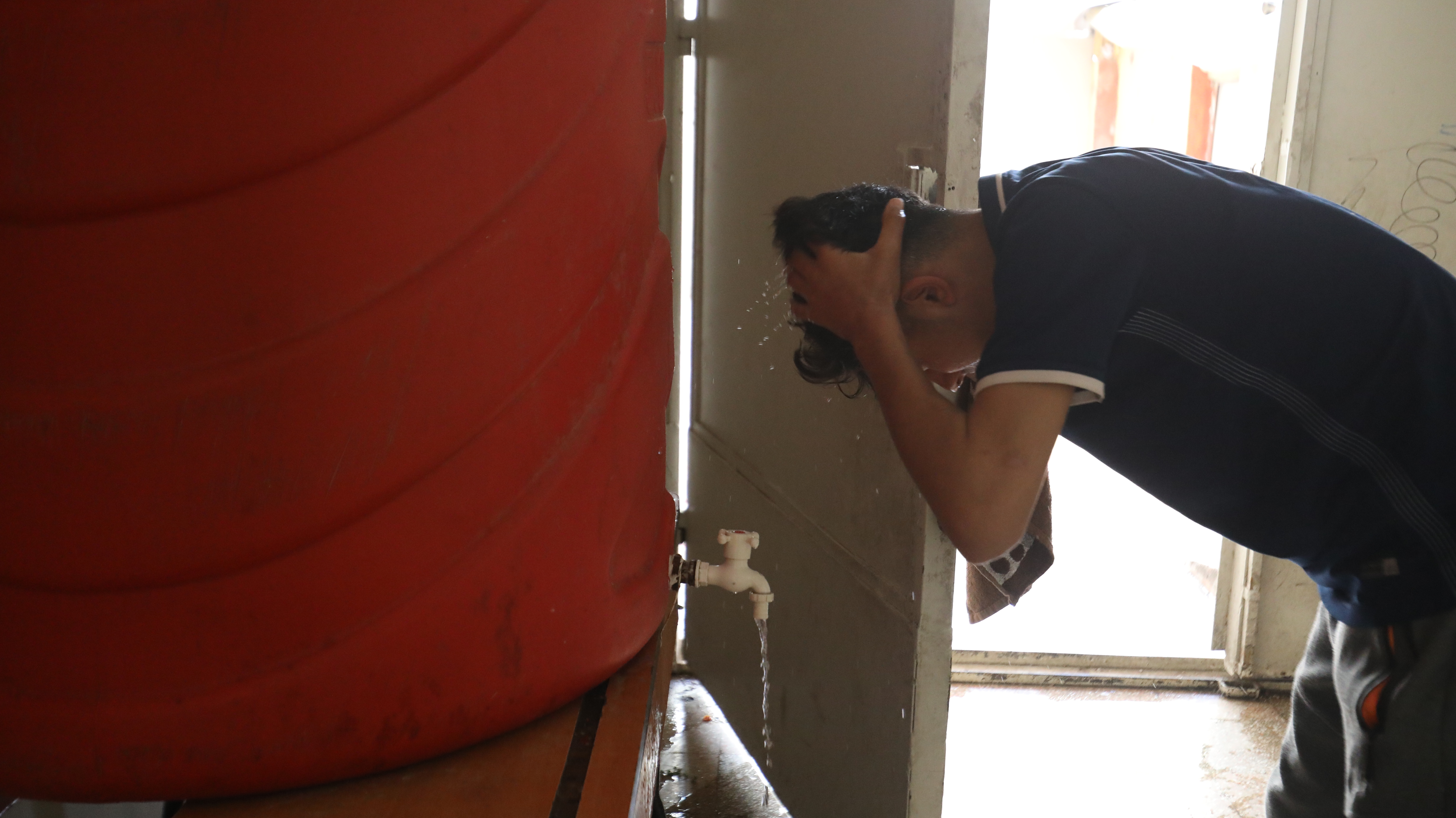 ein Junger Mann wäscht sich die Haare vor einem roten Wassertank