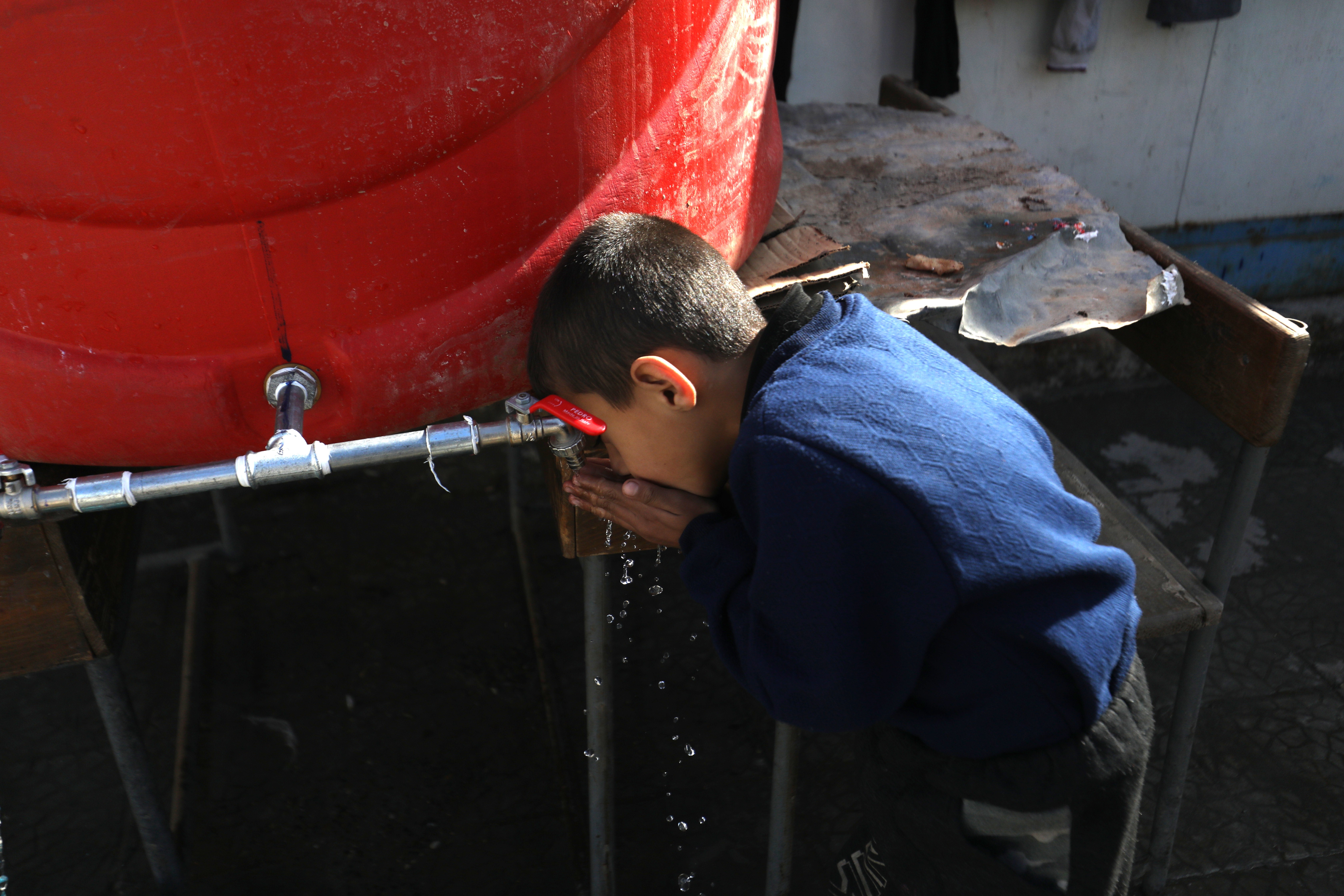Ein Junge trinkt direkt aus dem Hahn eines Wassertanks