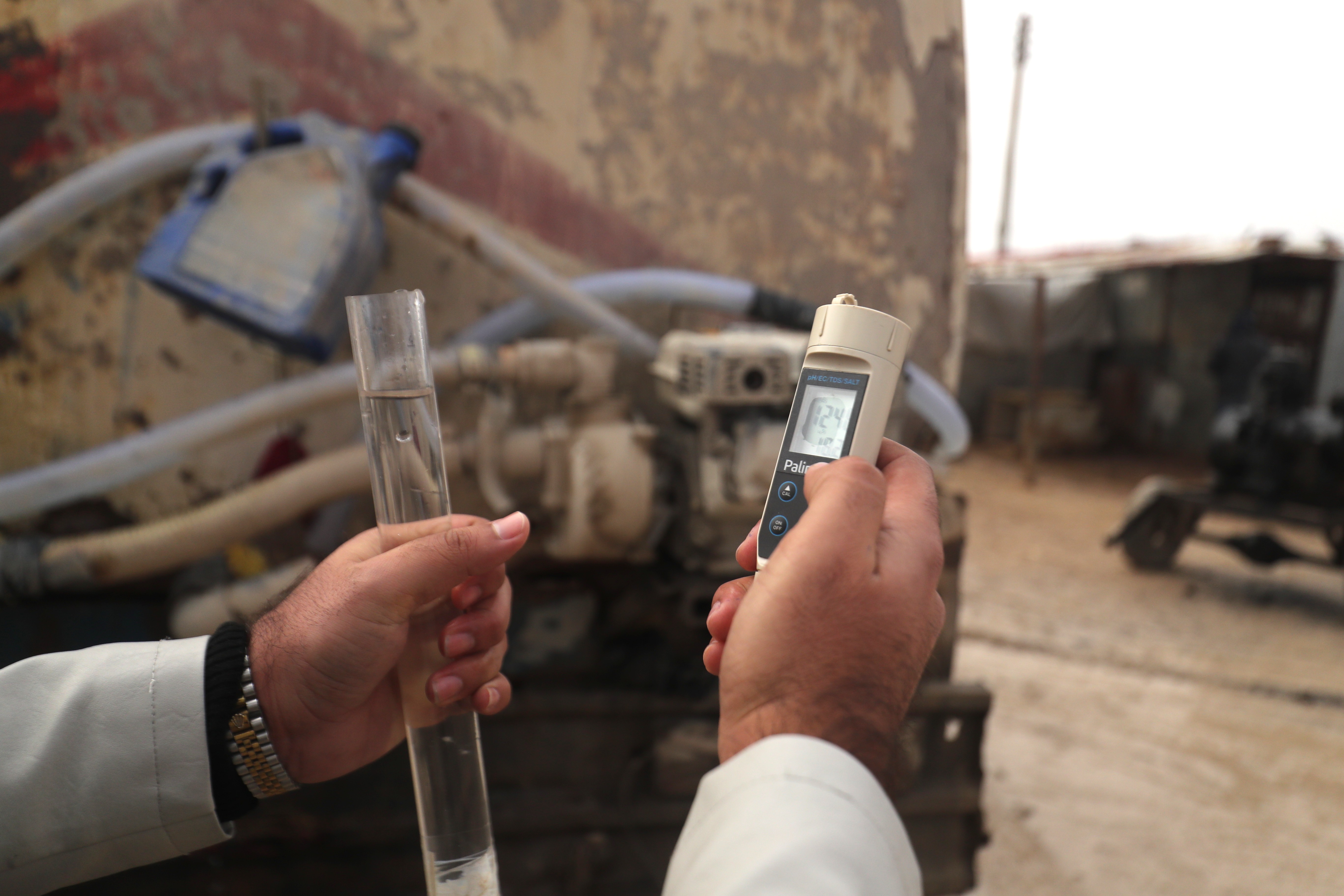 Nahaufnahme, eine linke Hand hält ein großes Reagenzglas, eine rechte Hand ein Messgerät