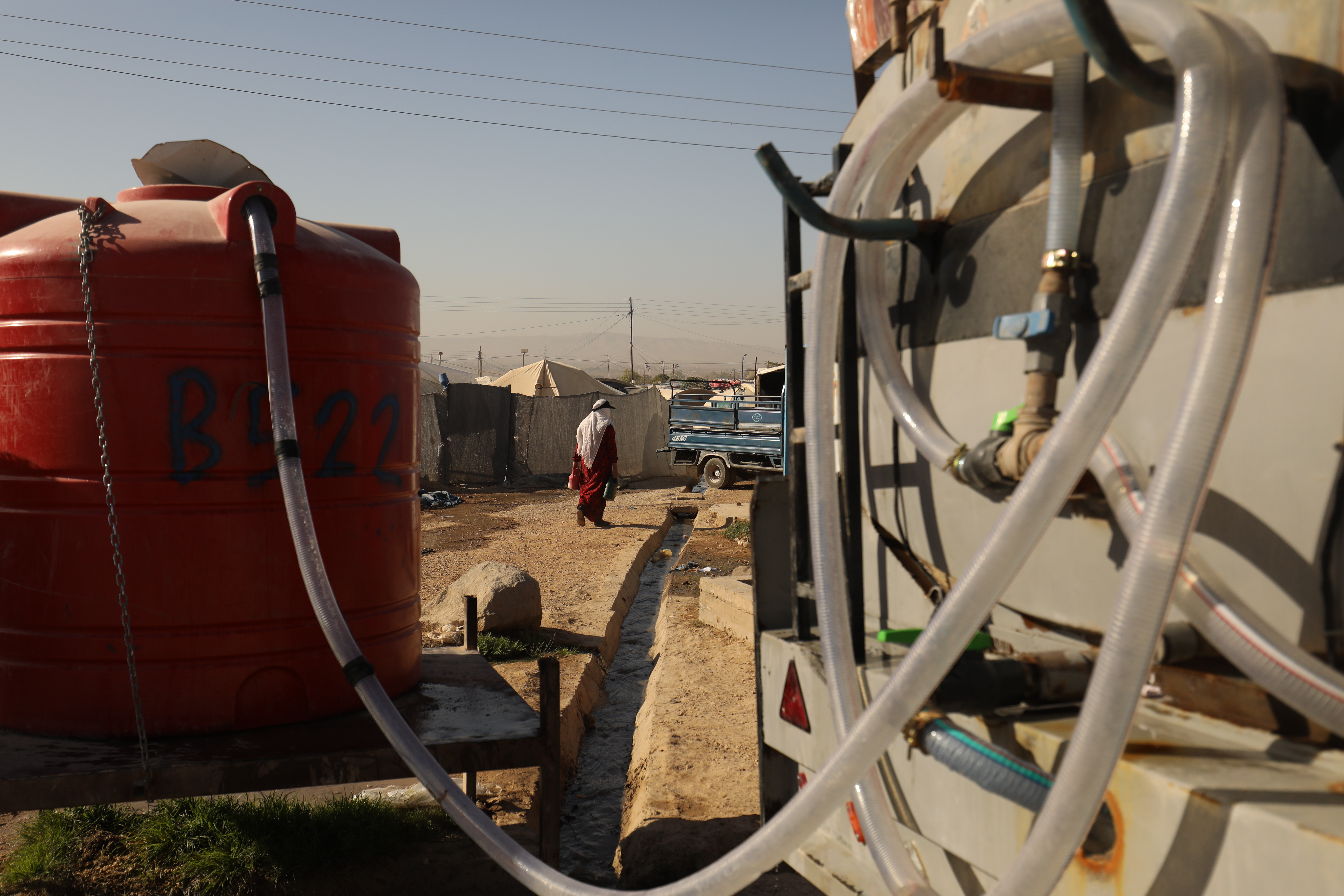 Rückseite eines LKWs rechts, von dort ein Schlauch zu einem Wassertanks links, im Hintergrund Zelte