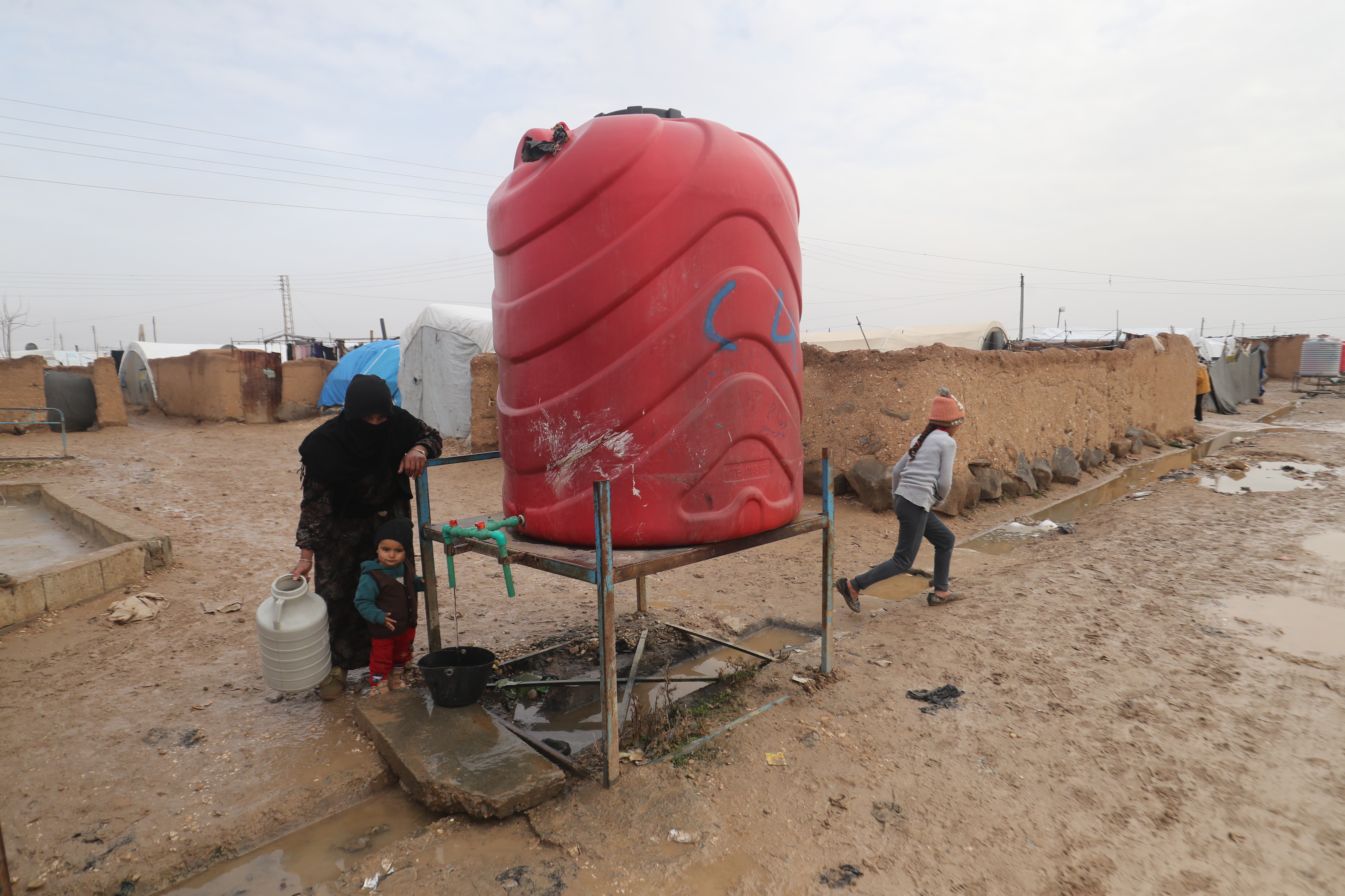 Roter Wassertank auf einem Gestell, eine Frau mit Kanister daneben