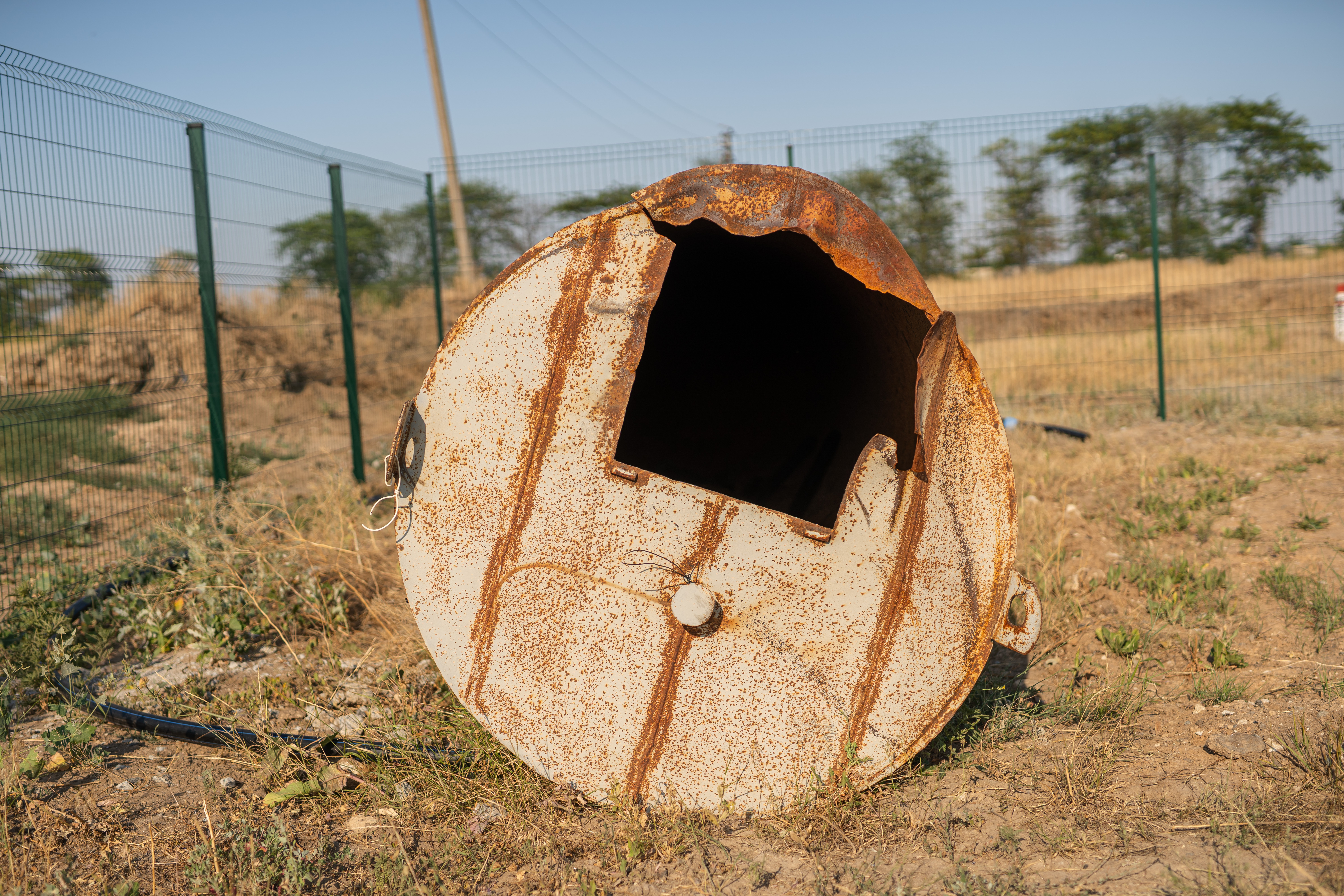 Das Bild zeigt einen alten, rostigen Wassertank, der auf einem Feld liegt.